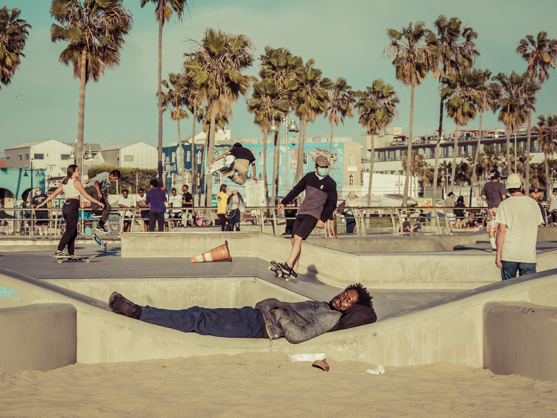 An exhausted man sleeps on the wall of the famous skate park on Venice Beach, oblivious to the noise and performance beside him