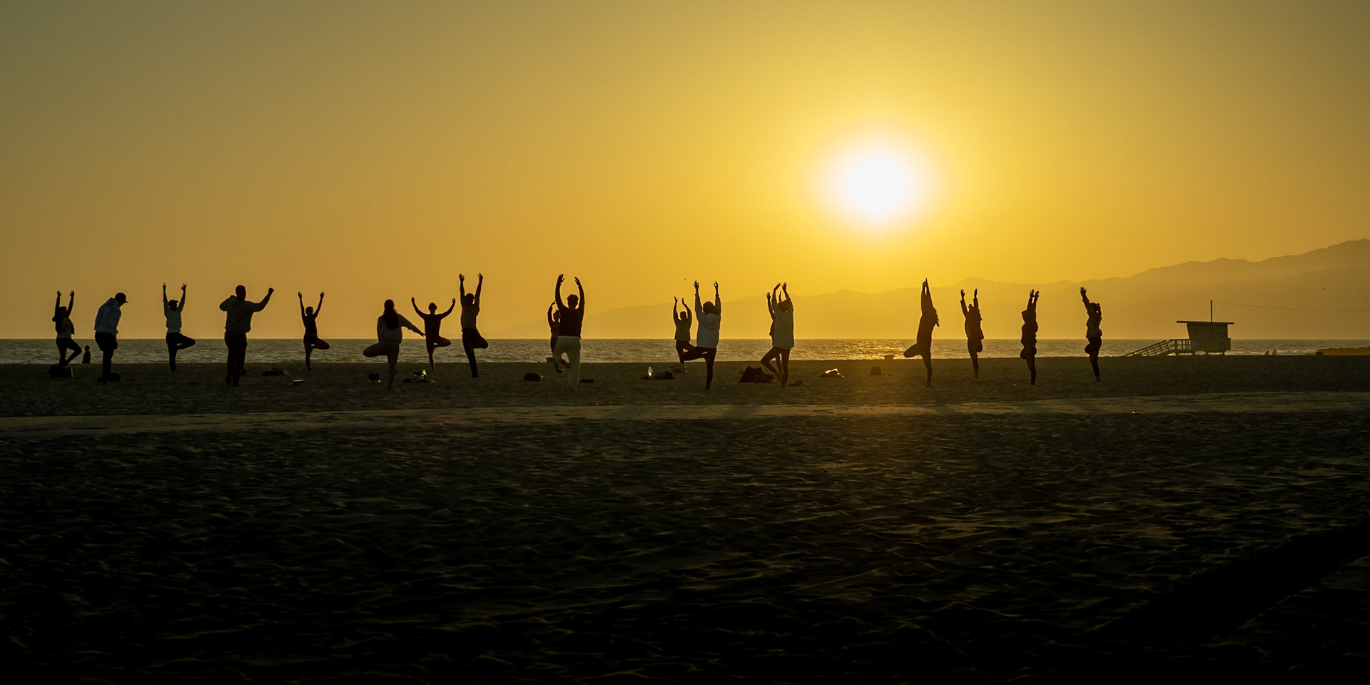 A group practice yoga on Venice Beach as sun sets behind the Santa Monica mountain range