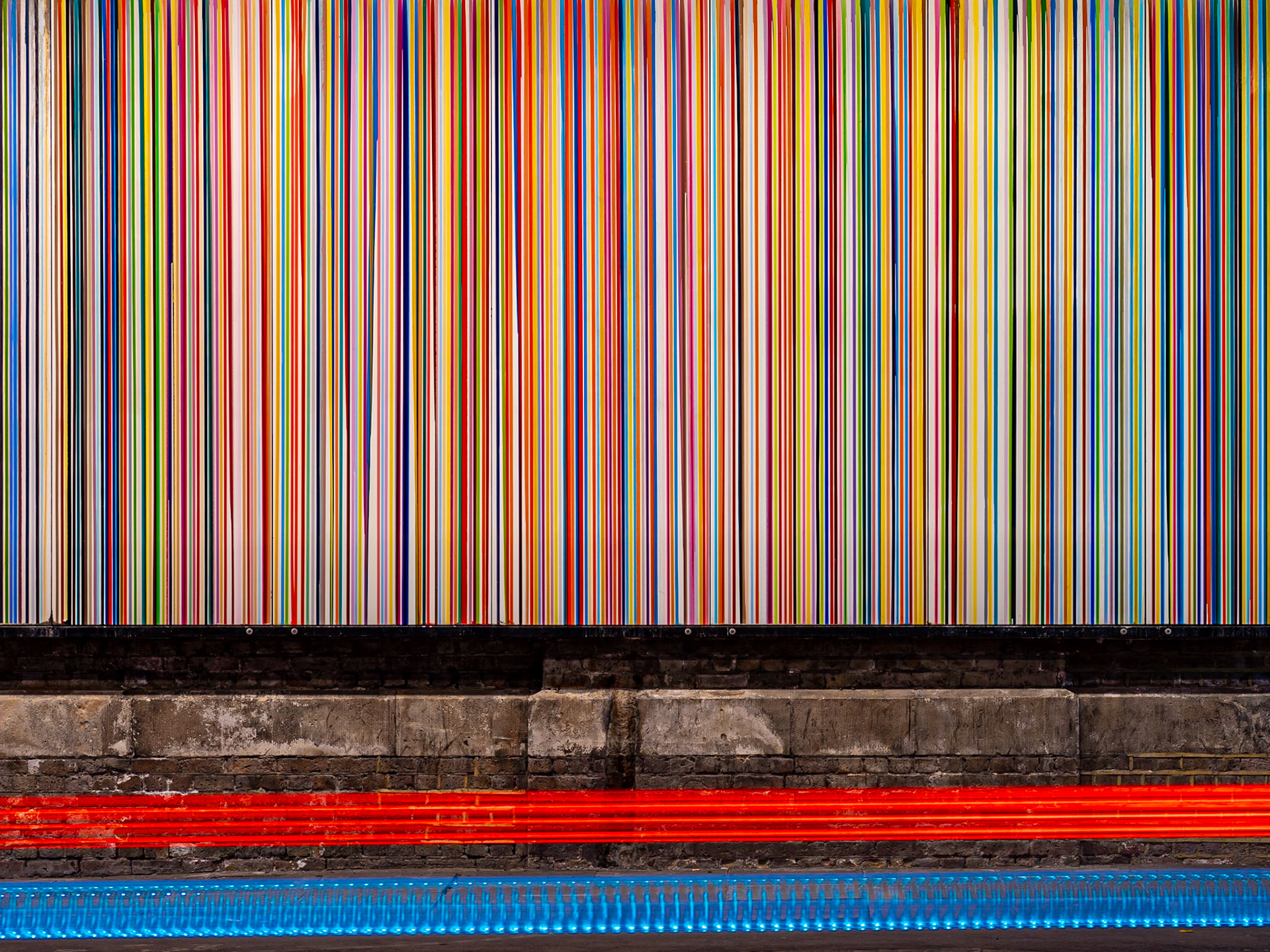 Passing traffic forms vivid light trails in front of a vibrant mural of lines in London