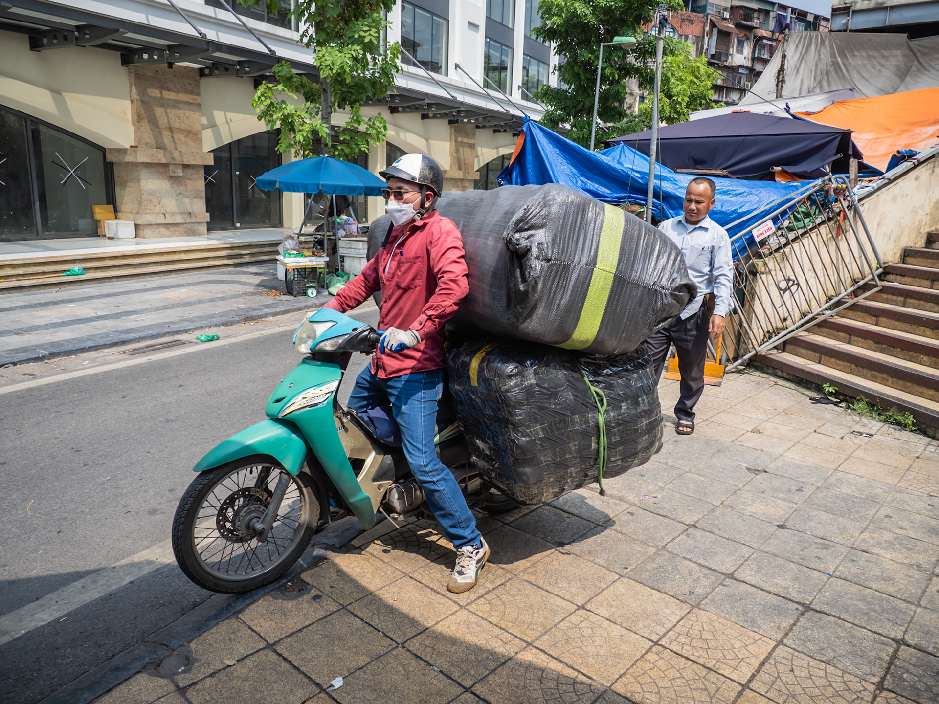 Masked and ready, a driver skillfully balances a massive, strapped-down load on his trusty moped, proving that in the Vietnamese city of Hanoi, the only limit is what you can keep upright