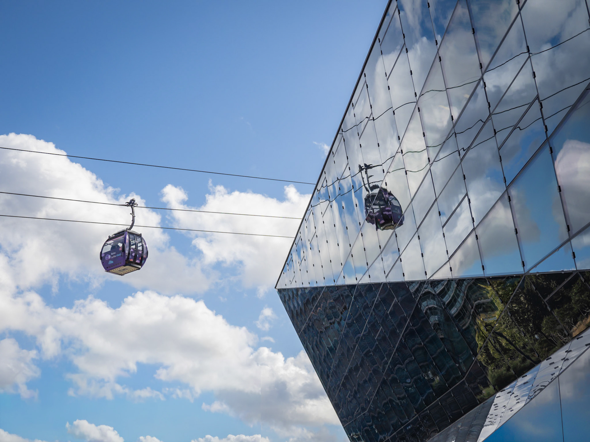 A cabin on London's cable car reflects against the mirrored glass of City Hall