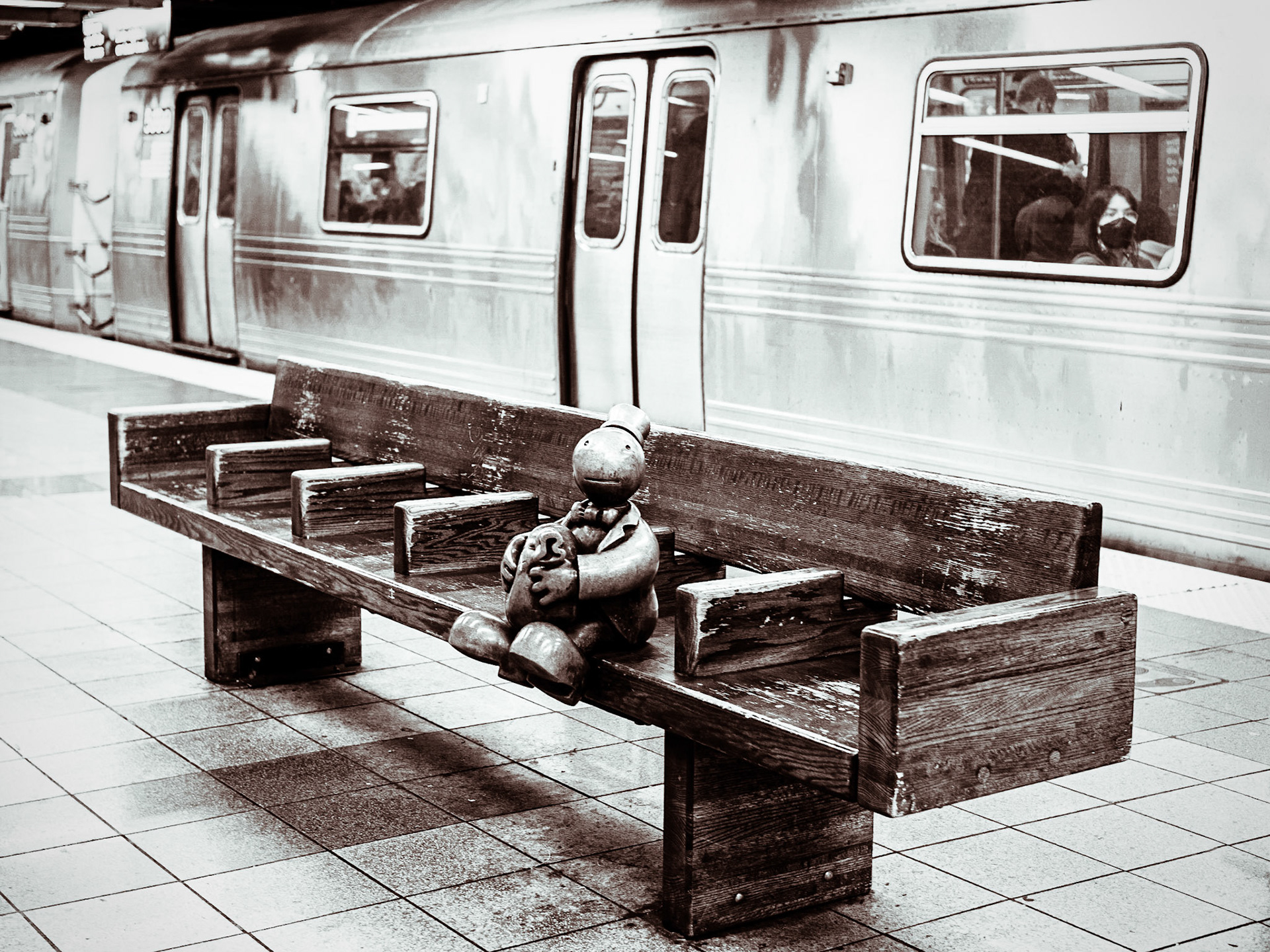 A bronze figure holds a figurative bag of cash as a subway train passes through the station