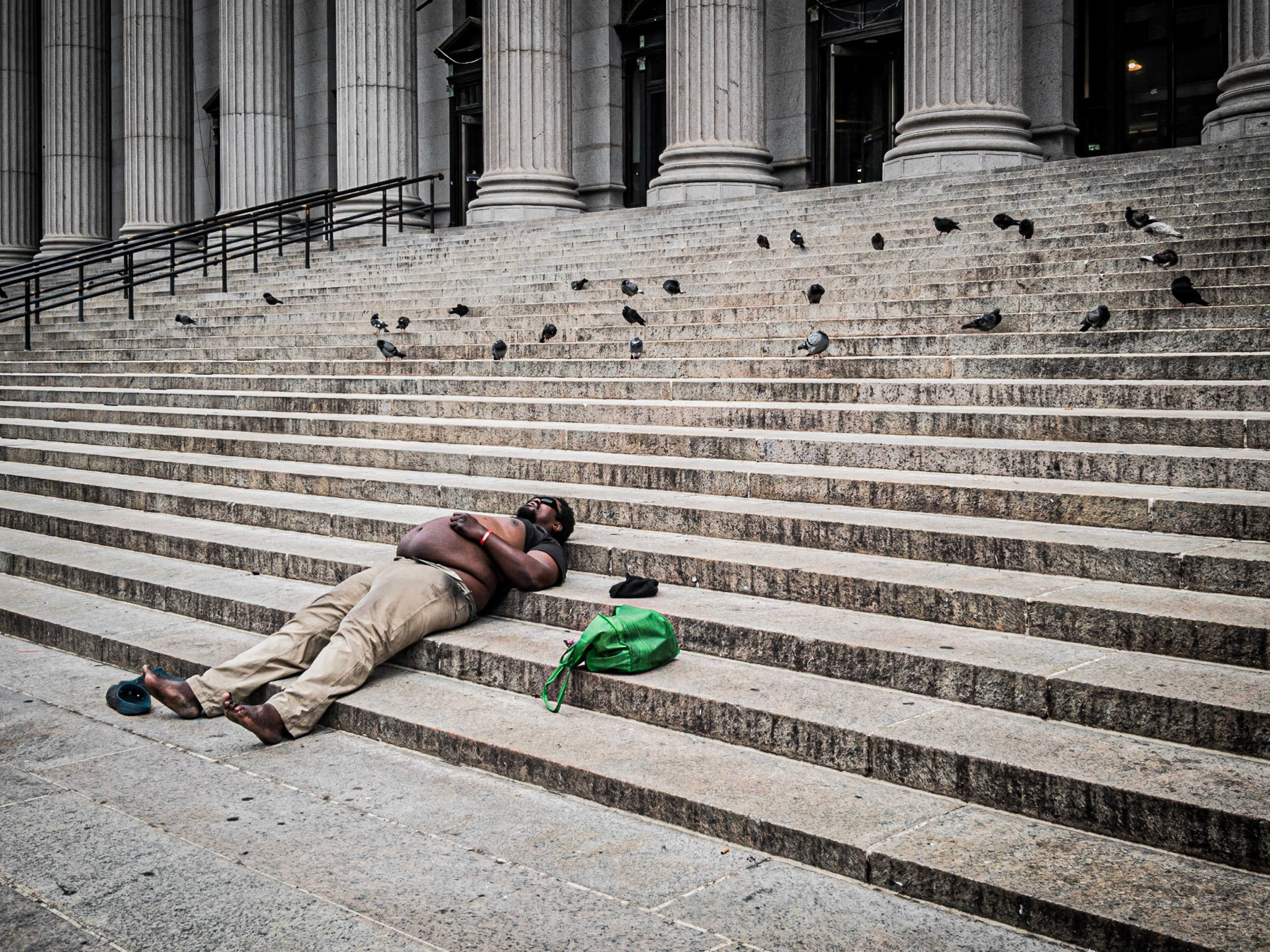 Local pigeons watch over a homeless man as he rests on the steps of the United States Post Office on 8th Avenue, Manhattan