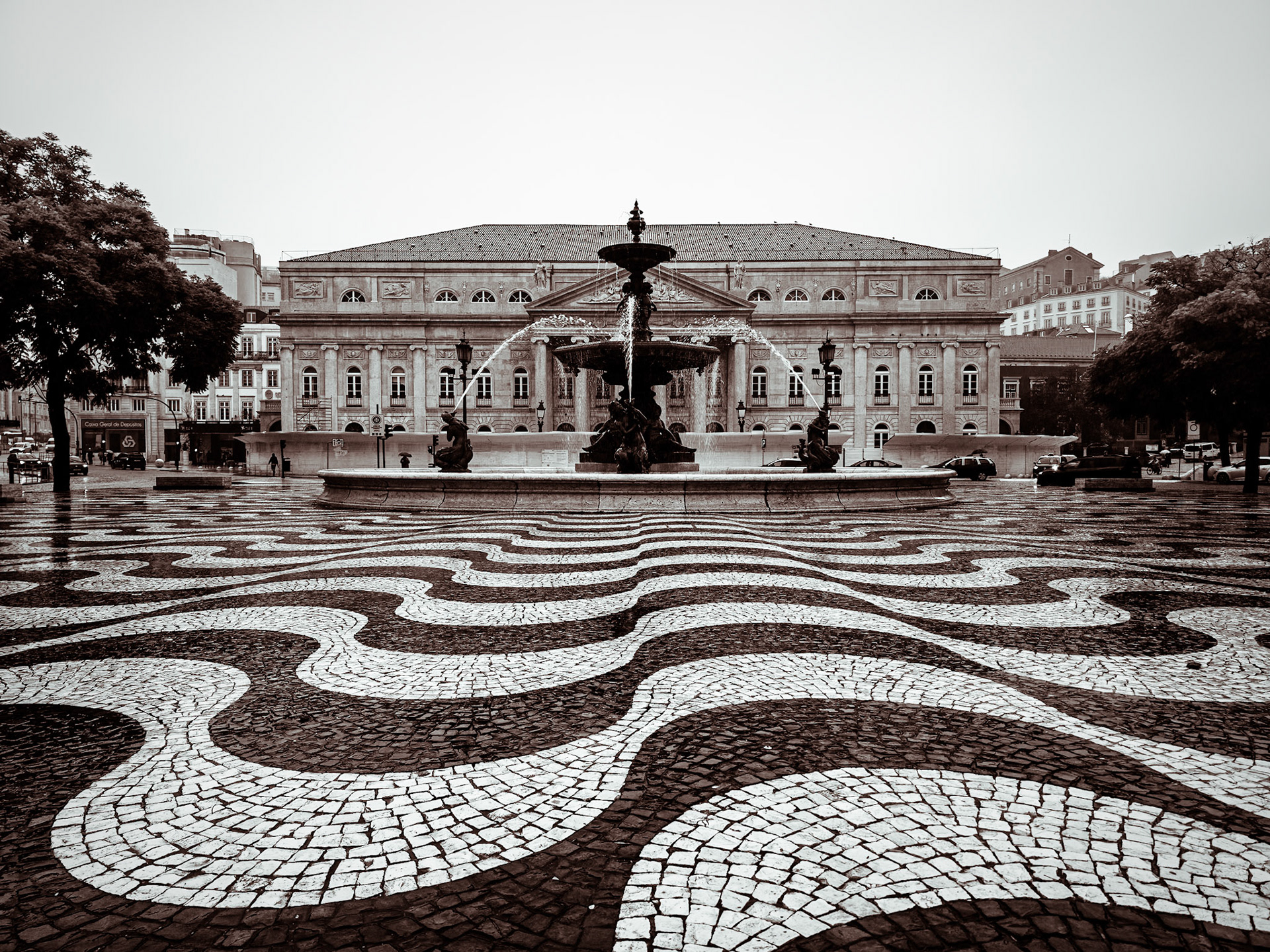 The distinctive wave-patterned cobblestones of Rossio Square spread out before an ornate central fountain in central Lisbon