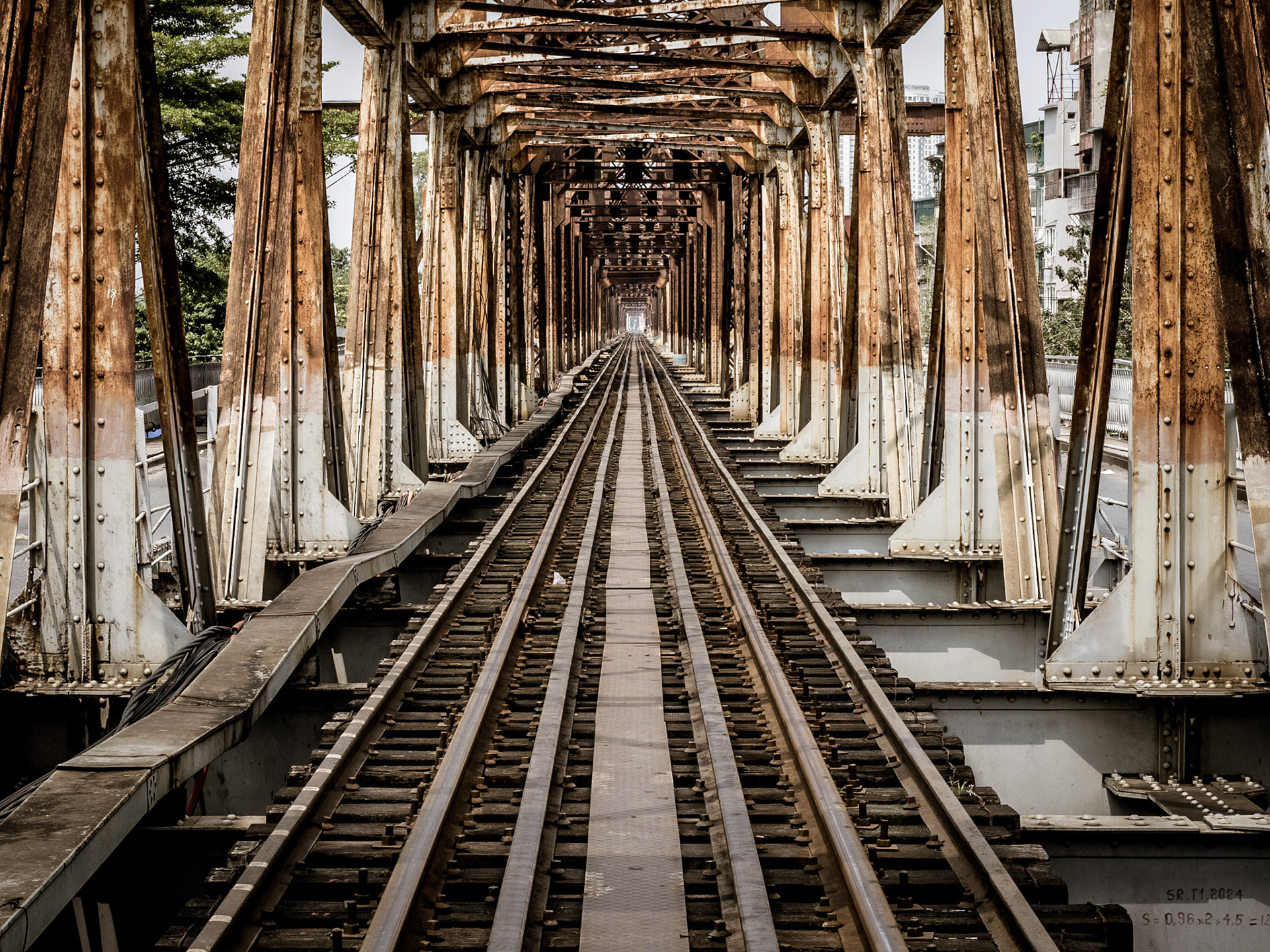 Rickety tracks fade in to the distance as the pass over the rusty ironwork of the Long Bien railway bridge in Hanoi  Vietnam