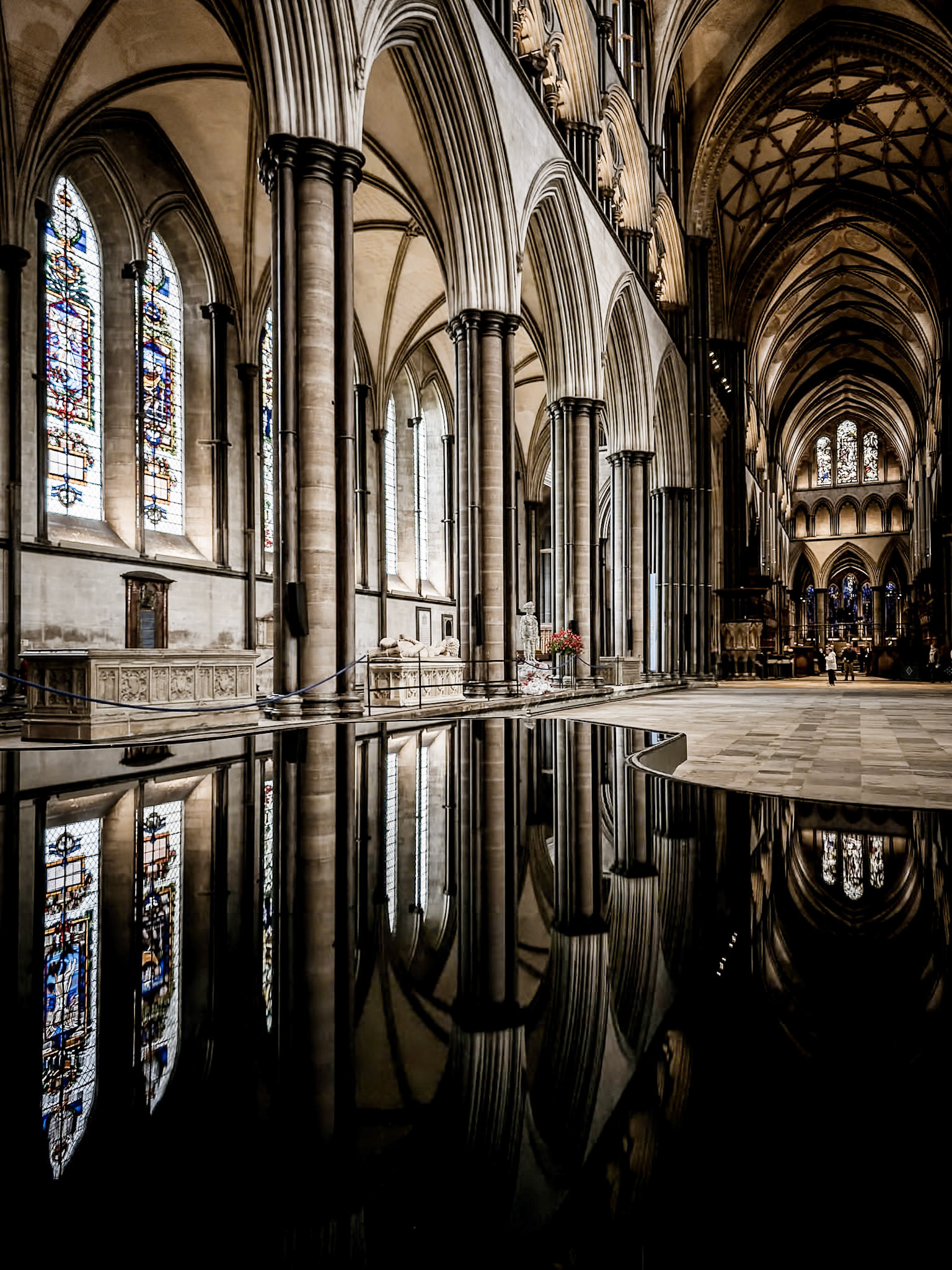 The calm surface of water in a font reflects the beautiful stained glasses windows and the ancient architecture of Salisbury Cahtedral