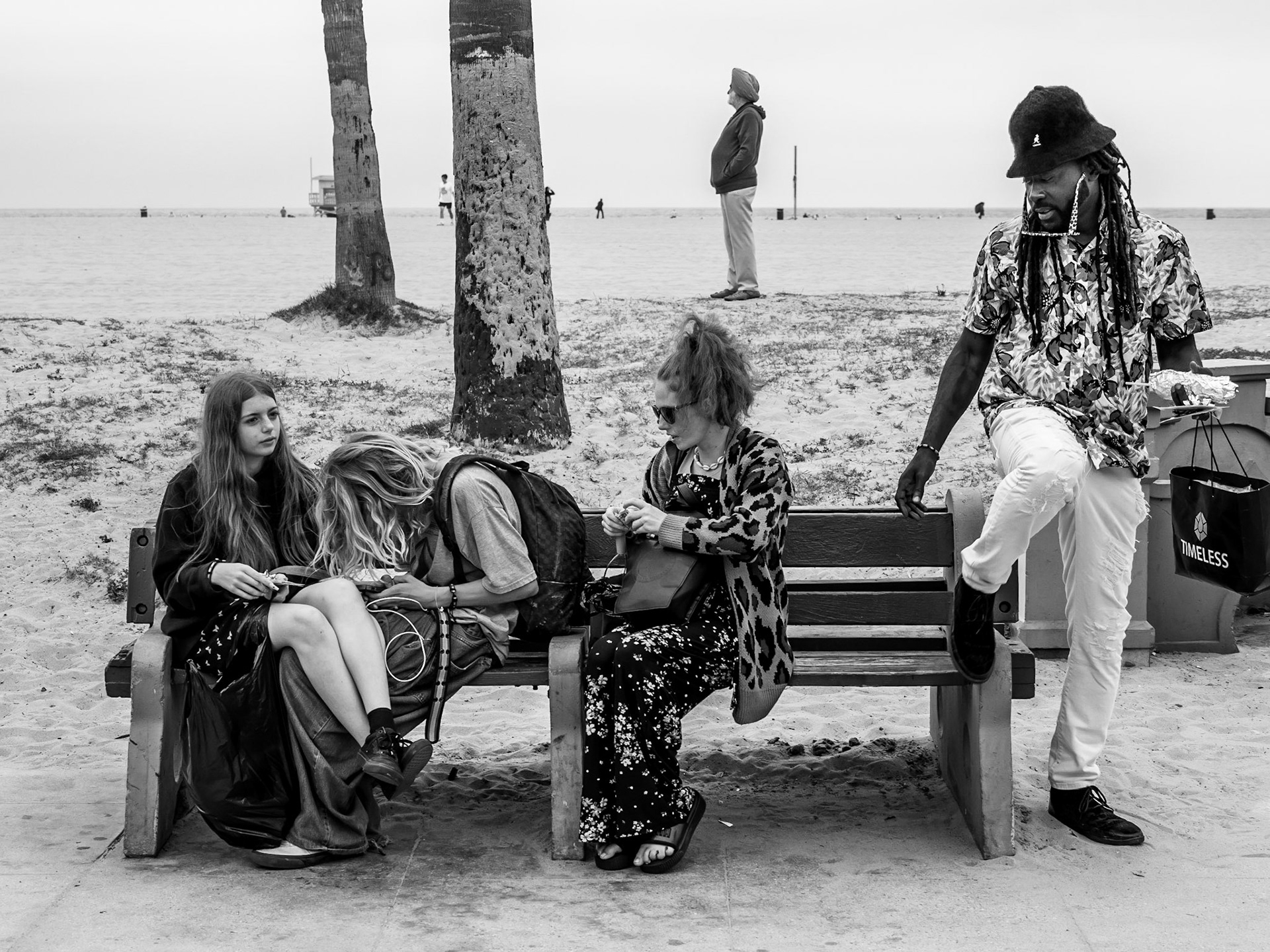 A young women catches-up on her notification whilst her friends wait, and a man look on