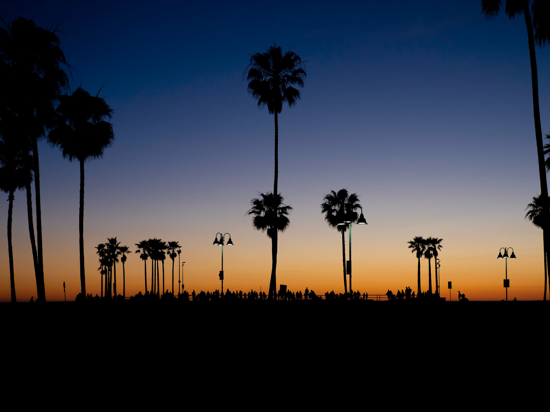 Spectators watch skateboarders performing their stunts and tricks as the sun sets behind the skatepark on Venice Beach in Los Angeles