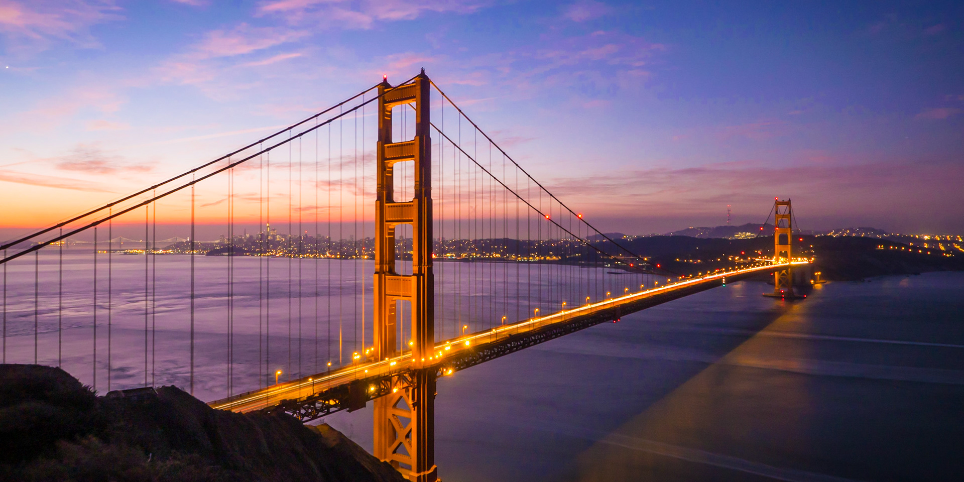 Traffic across the Golden Gate Bridge in San Francisco forms light trails as dawn rises behind