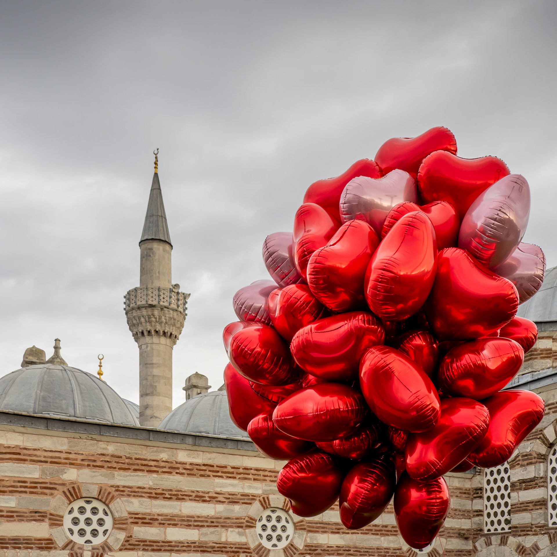 A large collection of red heart-shaped balloons float mid-air next to a mosque on the shore of the Uskudar district of Istanbul, Turkey