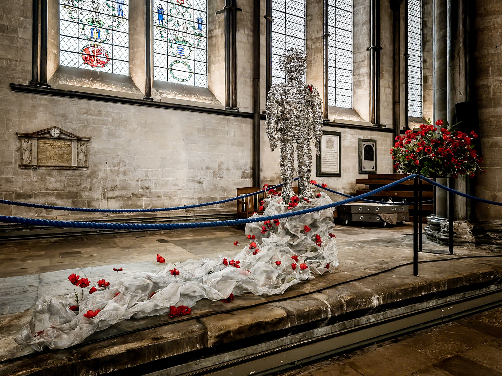 Crafted from delicate wire, a soldier stands in silent vigil, adorned with vibrant poppies, a poignant and modern tribute for those who have fallen