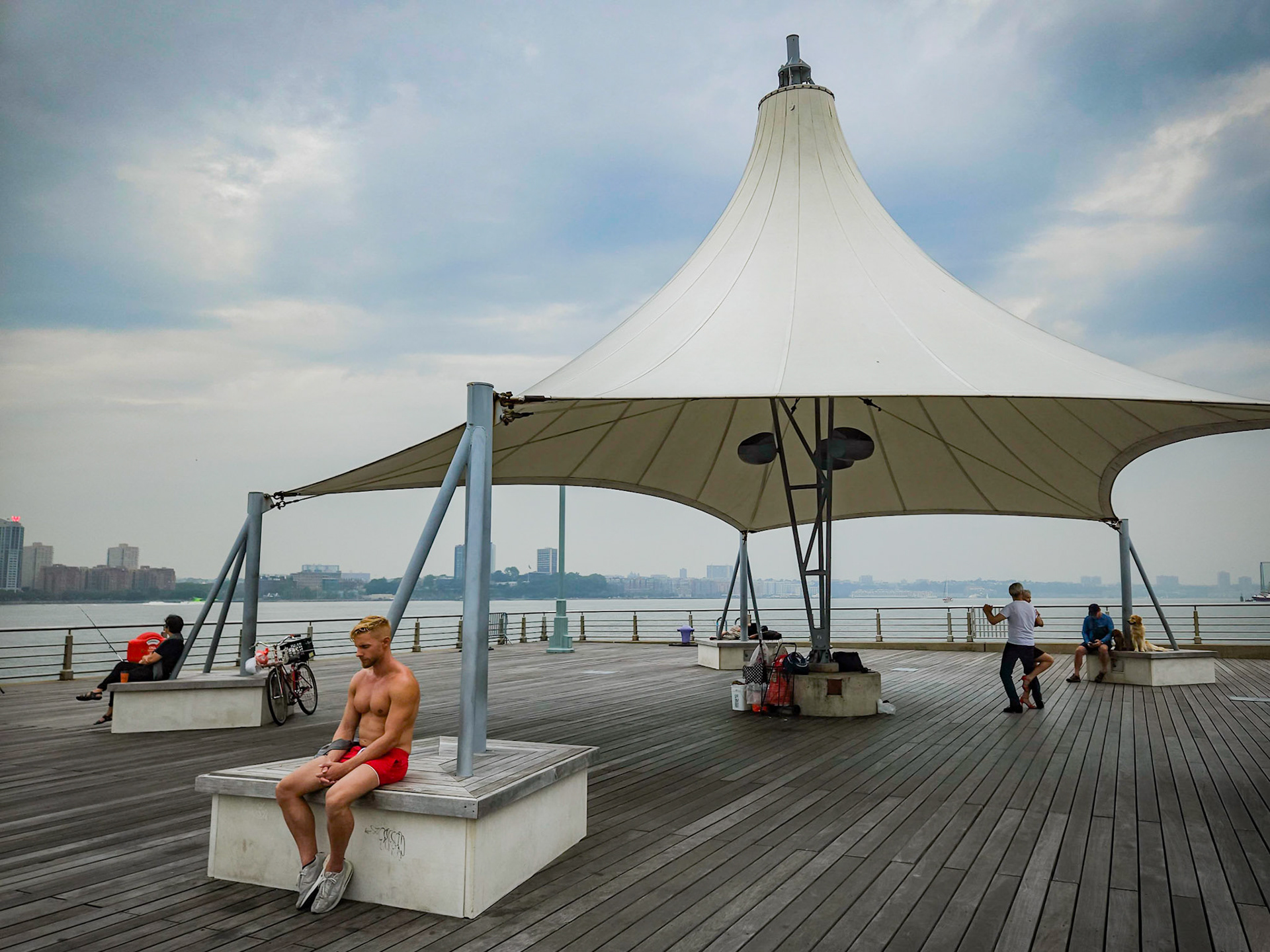 A runner meditates after his workout and a dog watches a couple dance the tango on the end of a pier jutting out into the Hudson river to the west of Manhattan, New York