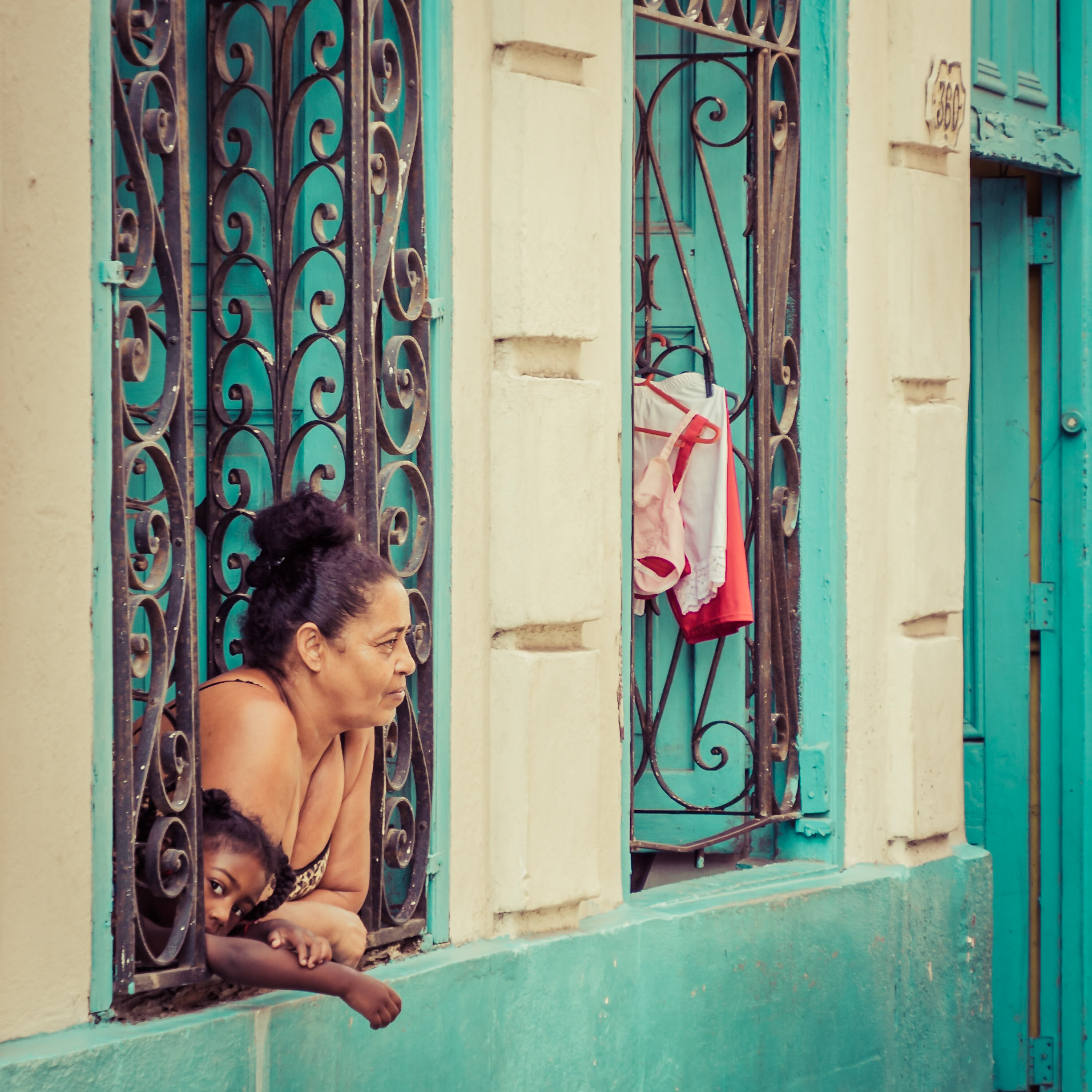 A young girl joins her mother to watch over the comings-and-goings in her street in Havana, Cuba