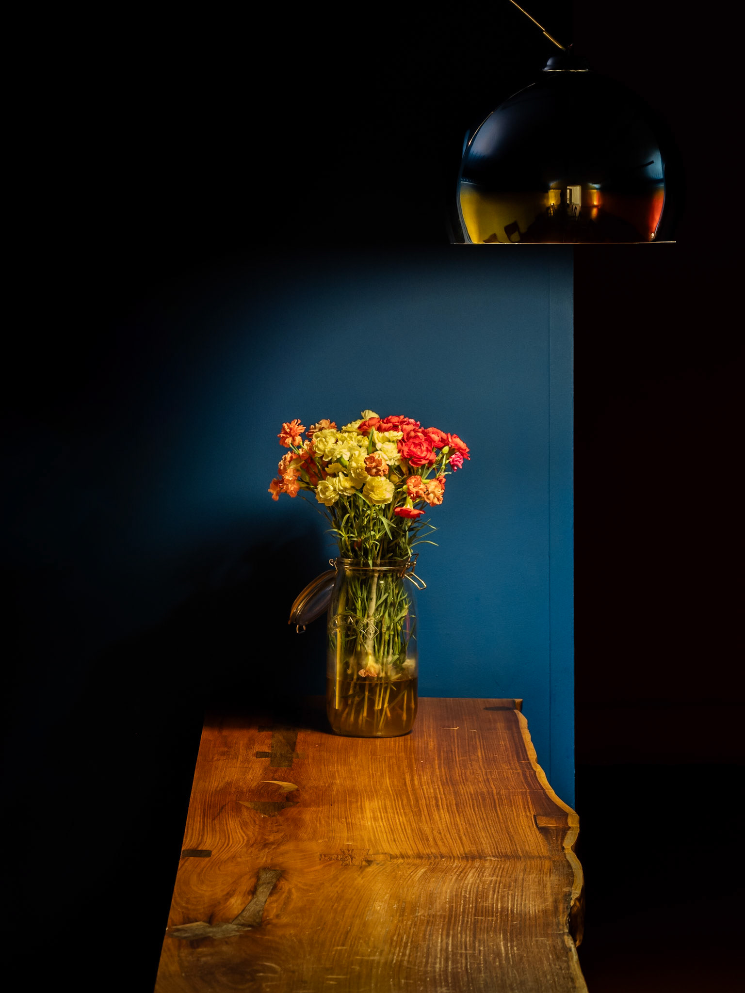 A collection of flowers sit in an old storage vase beneath a bronze lamp