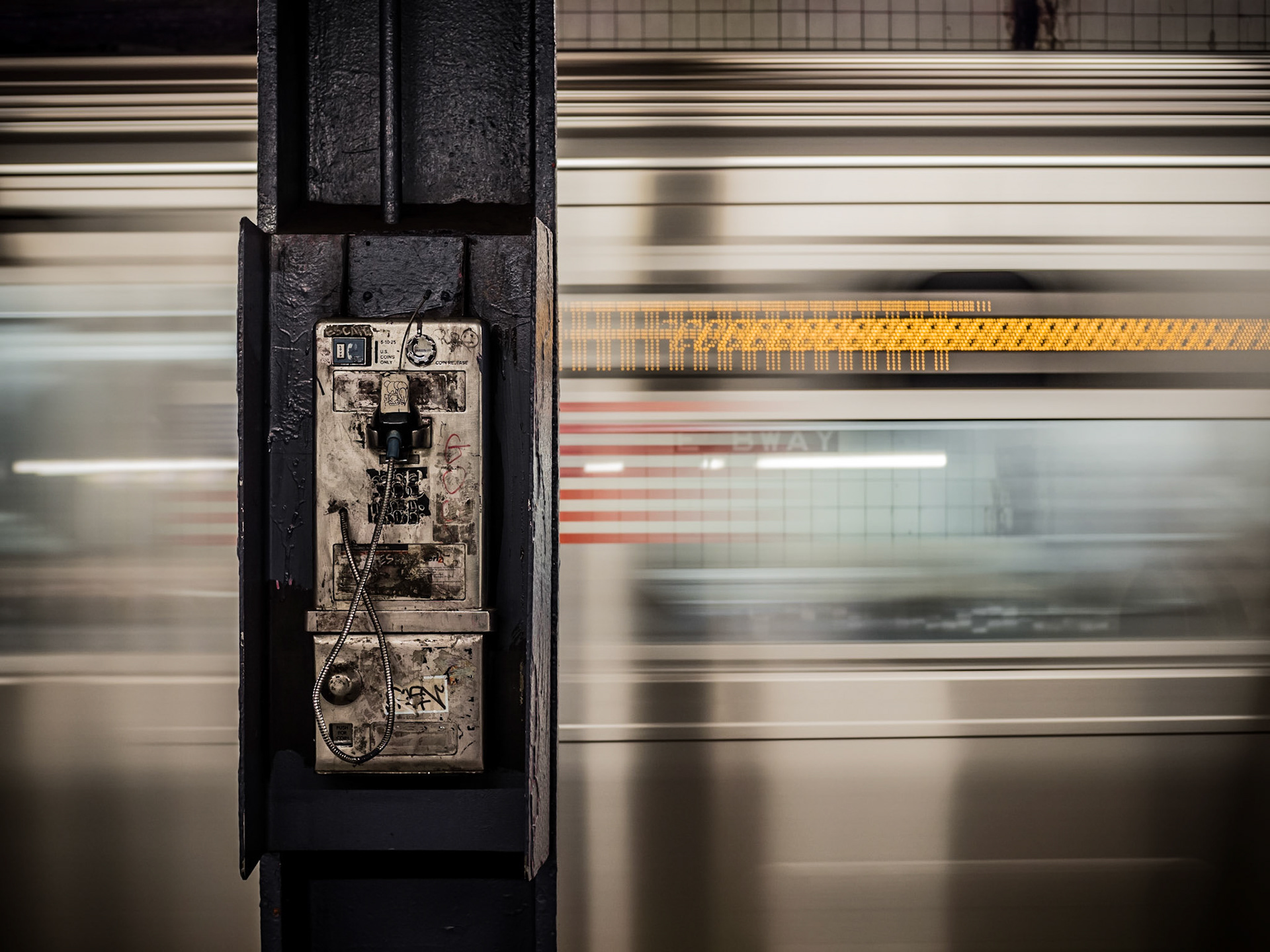 A subway train speeds past a payphone on the platform of East Broadway station in Manhattan, New York