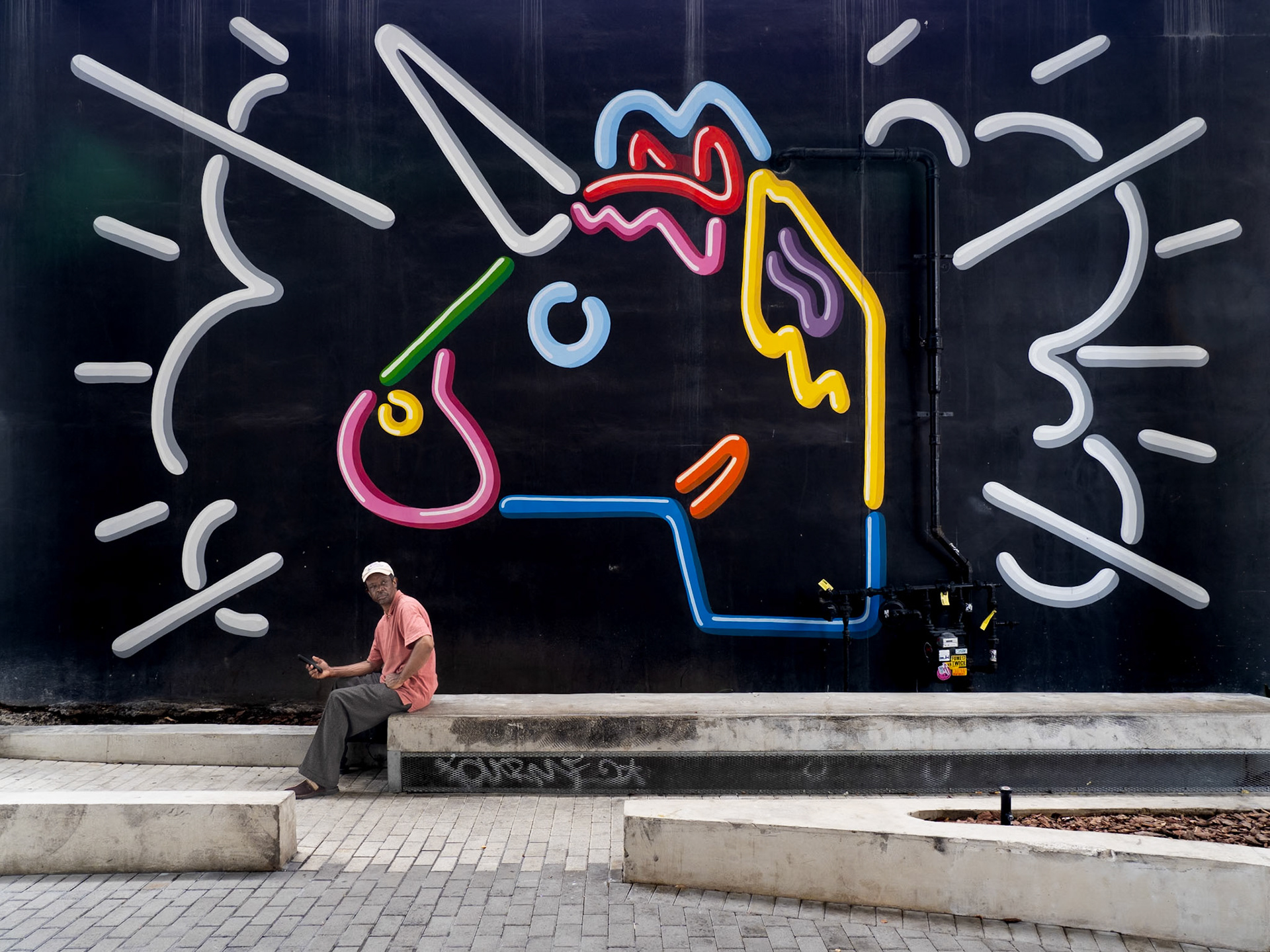 A local sits in front of a bright mural in the Wynwood district of Miami