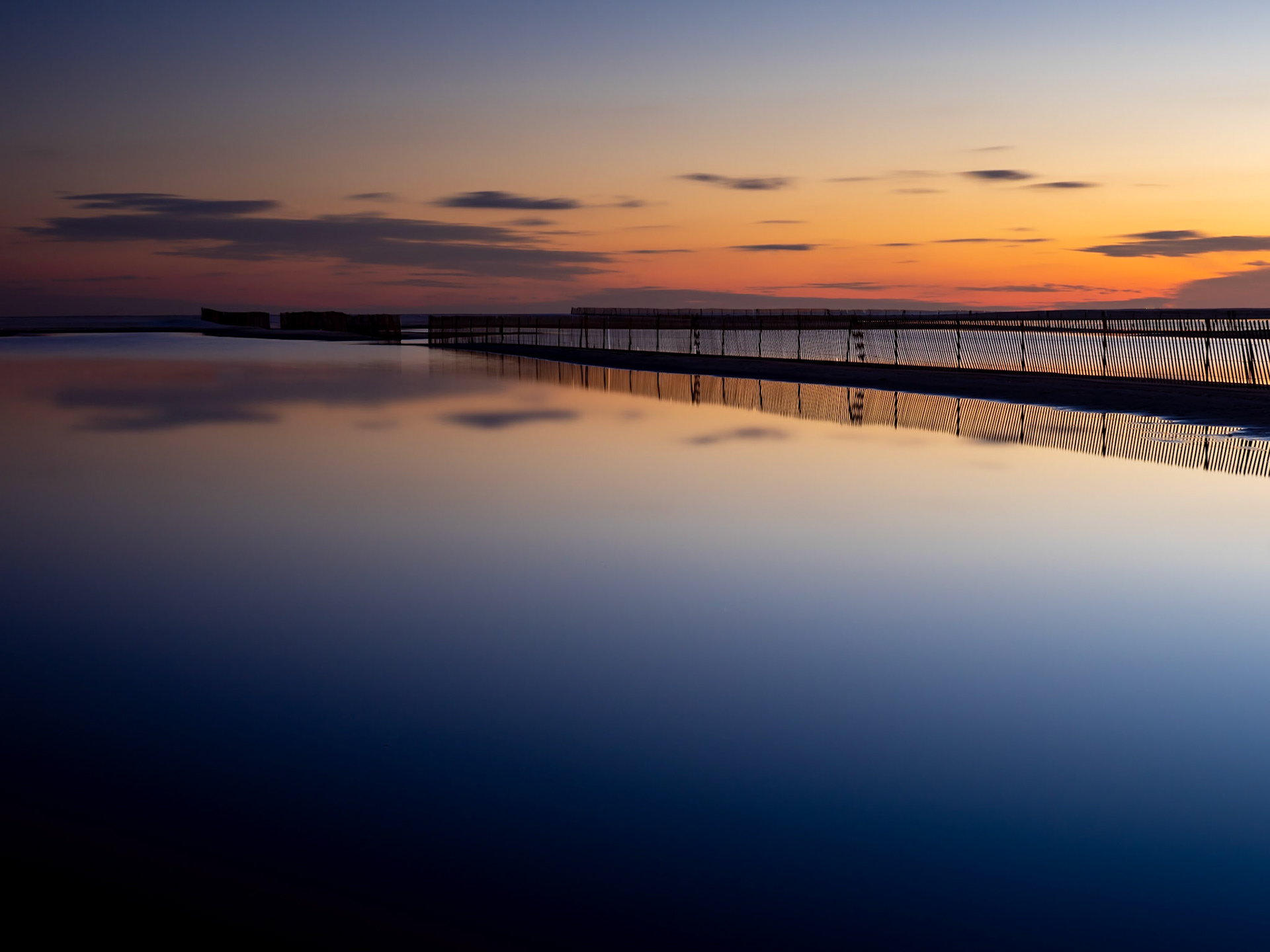 Vivid colours of the sun setting reflect on the surface of the shallow pool on Jones Beach