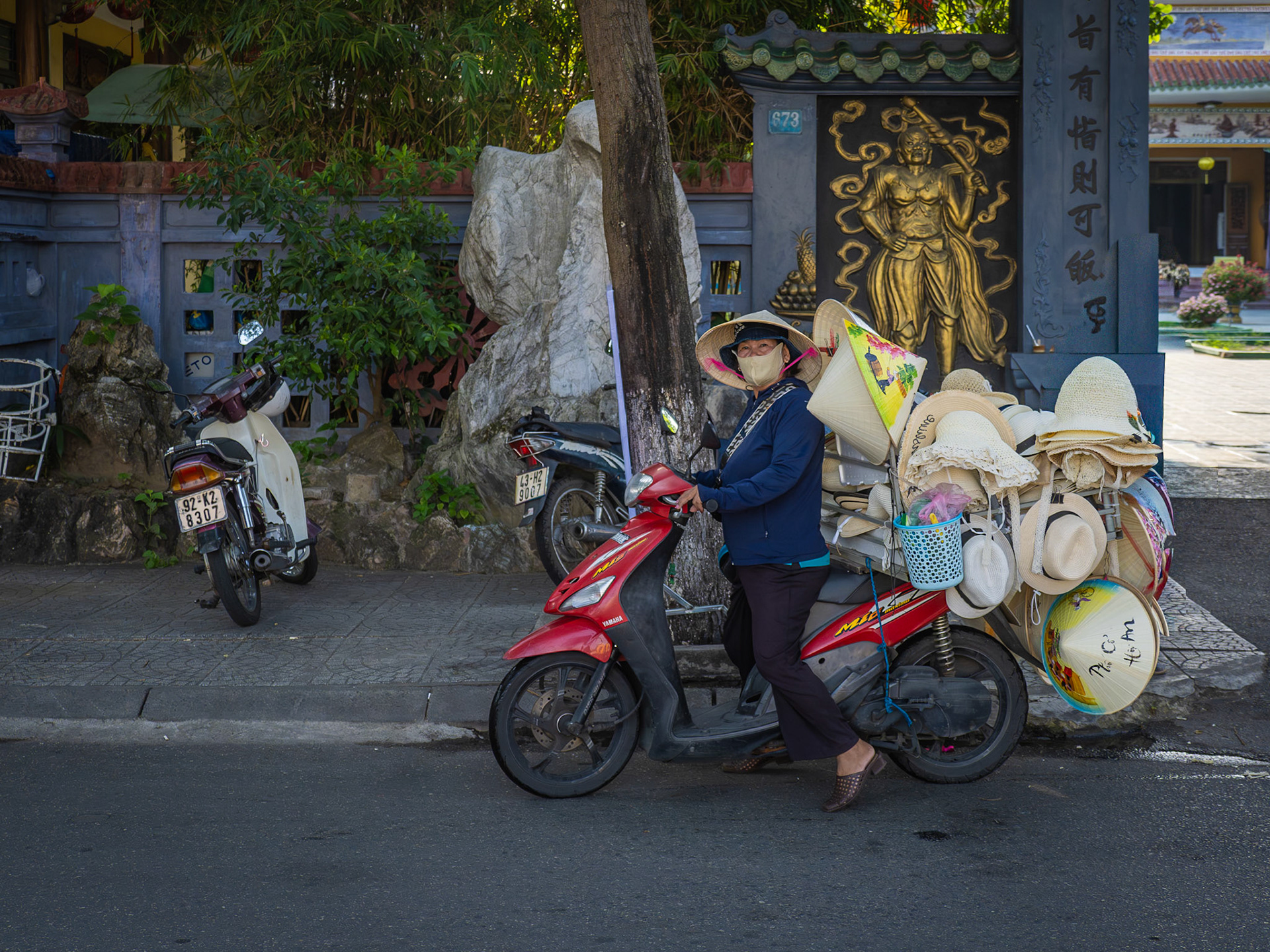A local woman sets off on her moped with her collection of traditional Vientamese Non La hats and other hats ready to sell on the streets of the ancient Vietnamese town of Hoi An