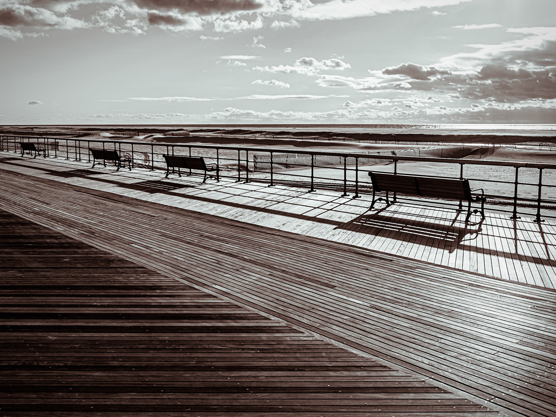 The bright sky casts stark shadows on a deserted boardwalk on Jones Beach