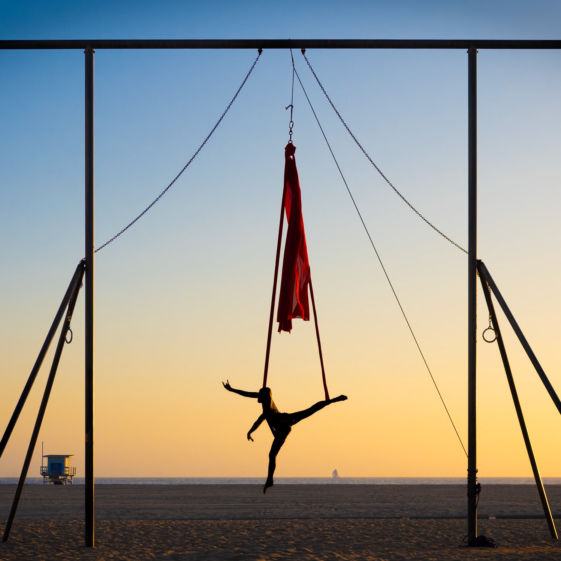An aerial silk artist performs on Santa Monica Beach as the sun sets behind her