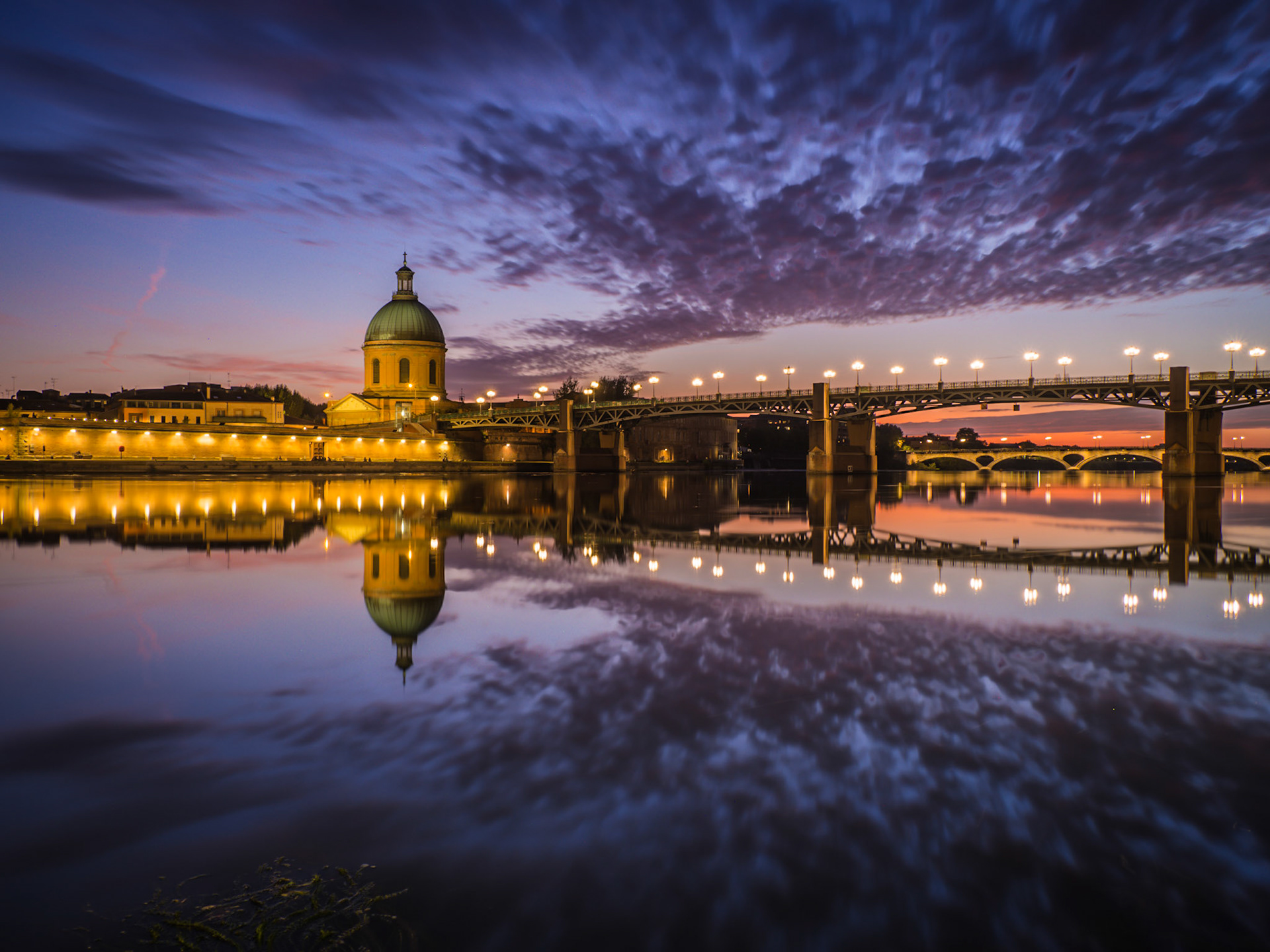 A stunning sunset is mirrored off the perfectly still waters flowing under the Saint Pierre Bridge in Toulouse