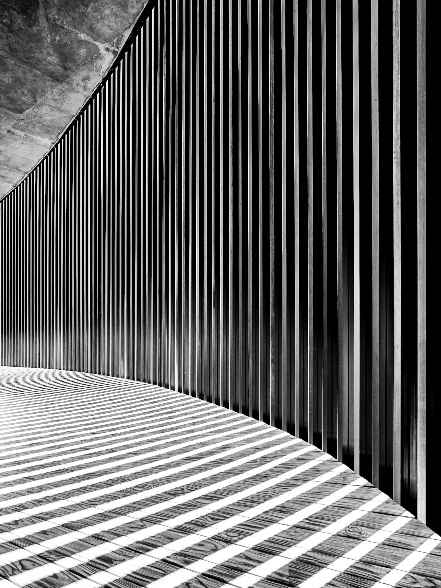 A setting sun shines through a grilled wall onto wooden planks