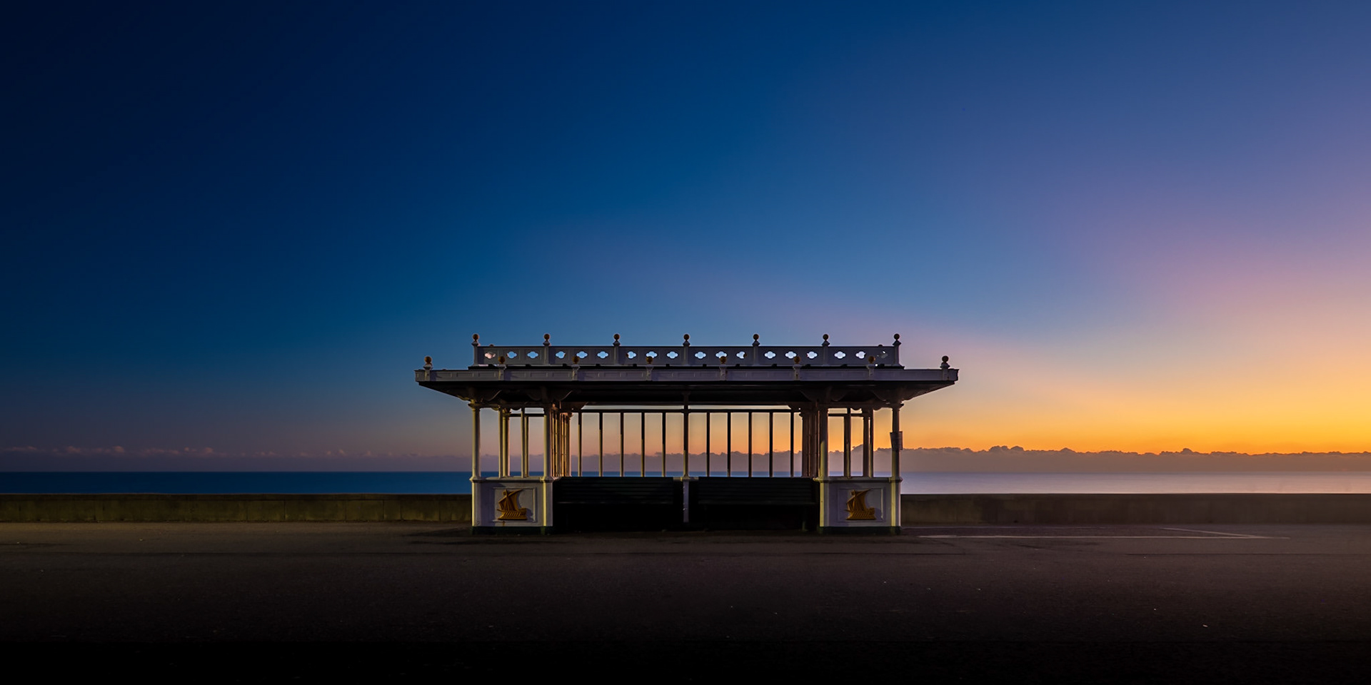 A spectrum of colours appears above a layer of cloud as the sun sets behind a shelter on the beach in Hove in Sussex