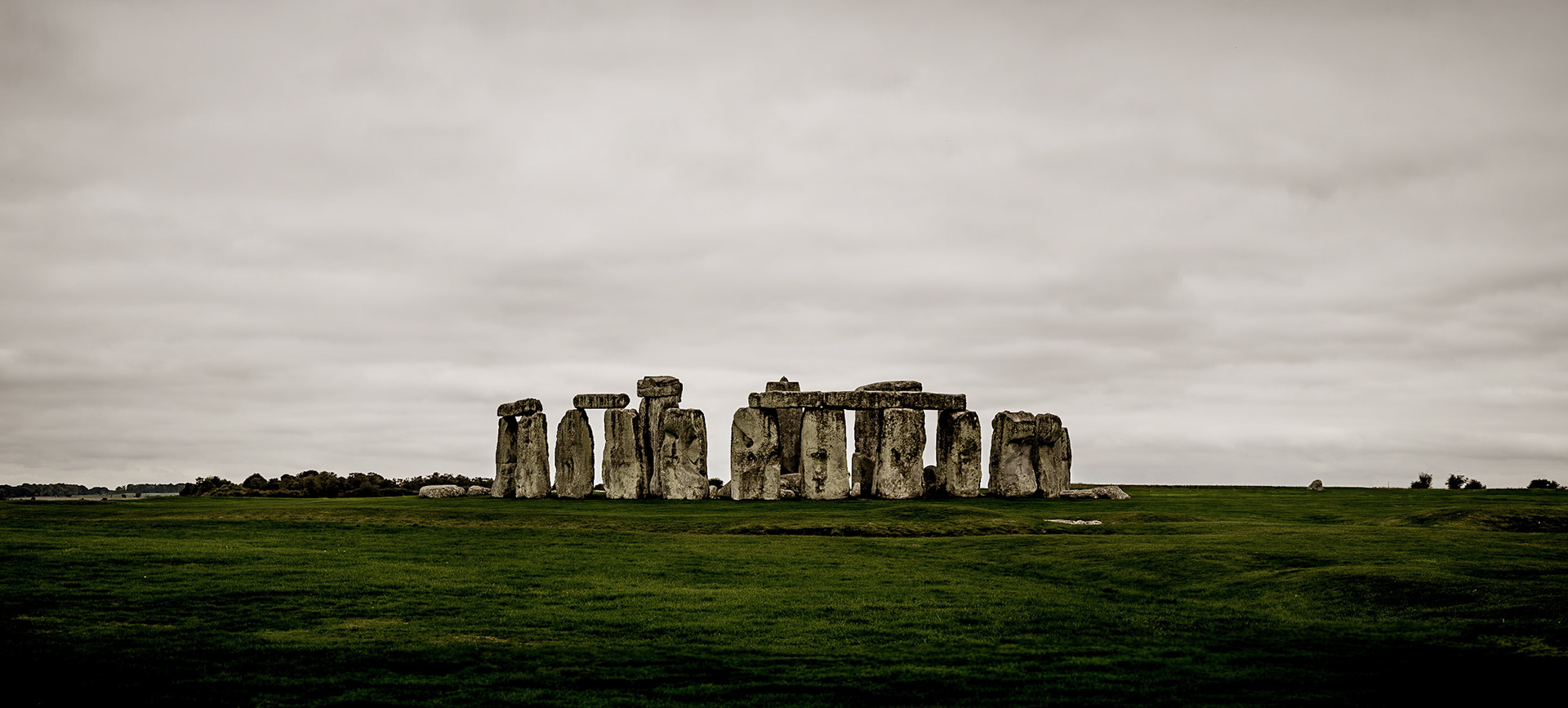 A palpable, ancient hush settles over Stonehenge, the immense stones anchoring the earth beneath a low, dramatic ceiling of grey, moody cloud