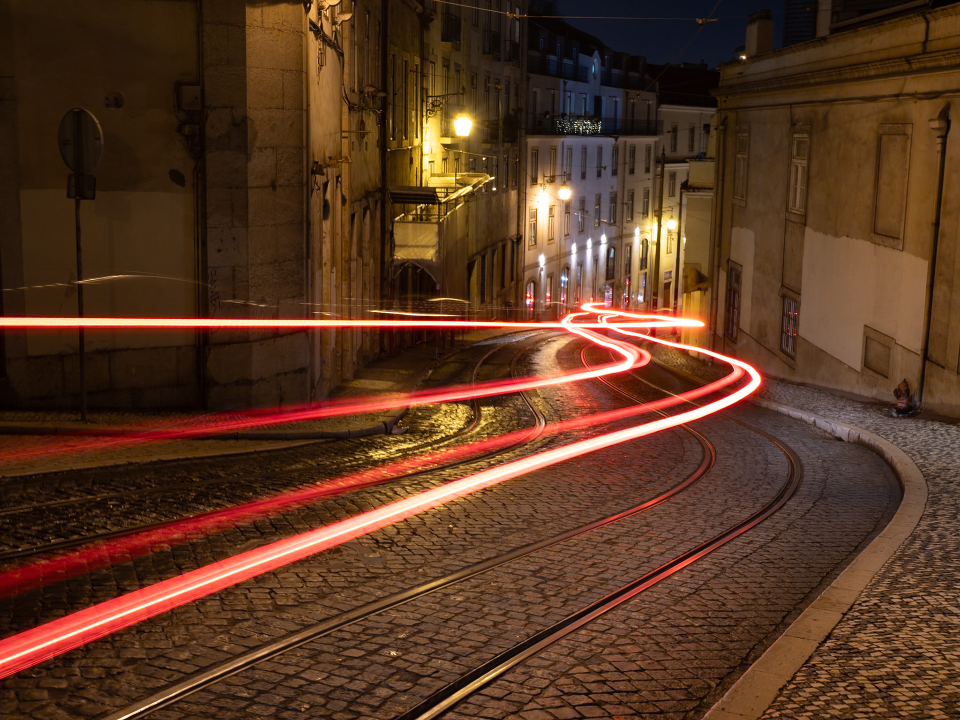 Red taillights streak along the tram rails, illuminating a quiet Lisbon night in a wave of motion