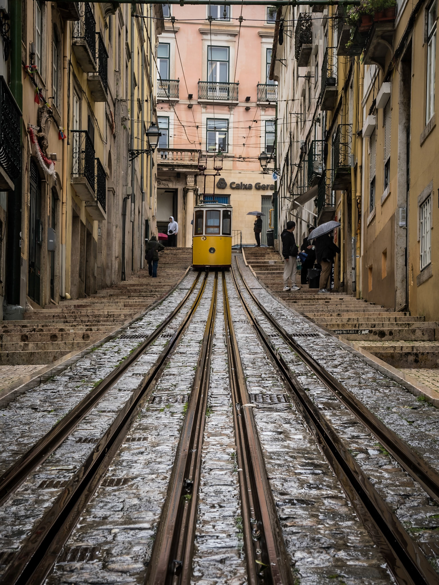The Bica funicular makes its steady ascent up a narrow, cobbled residential lane