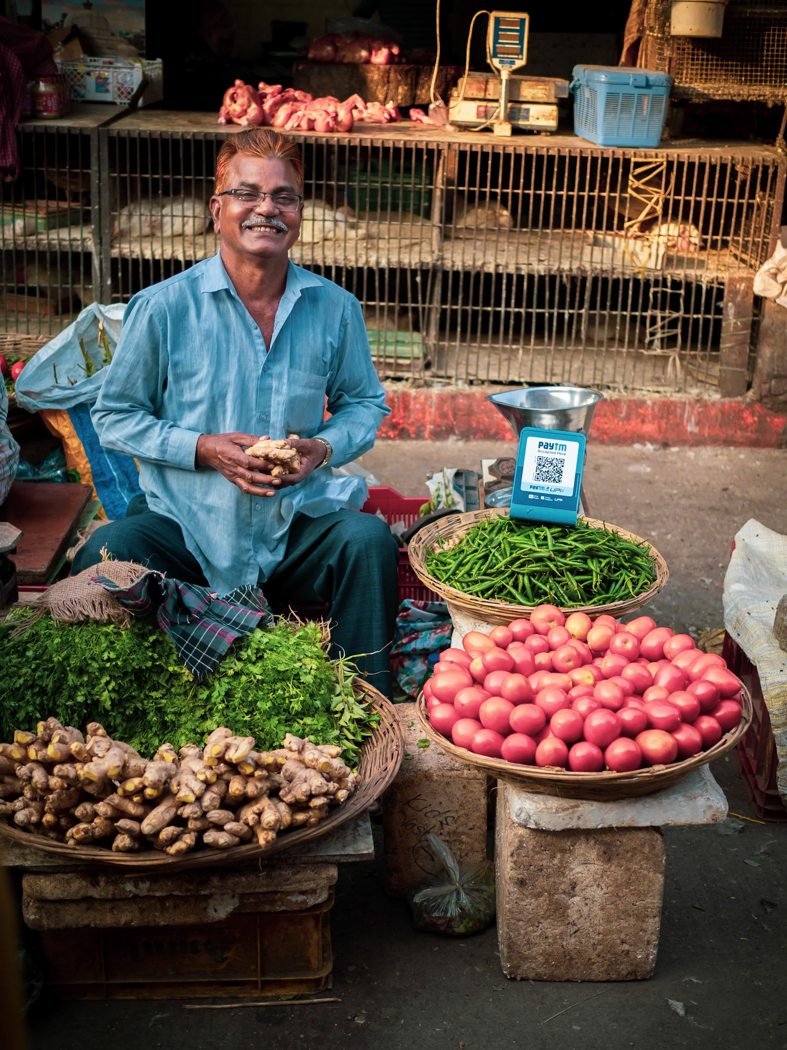 A ginger-haired market seller greets a new potential customer, selling, amngst other vegetables, ginger