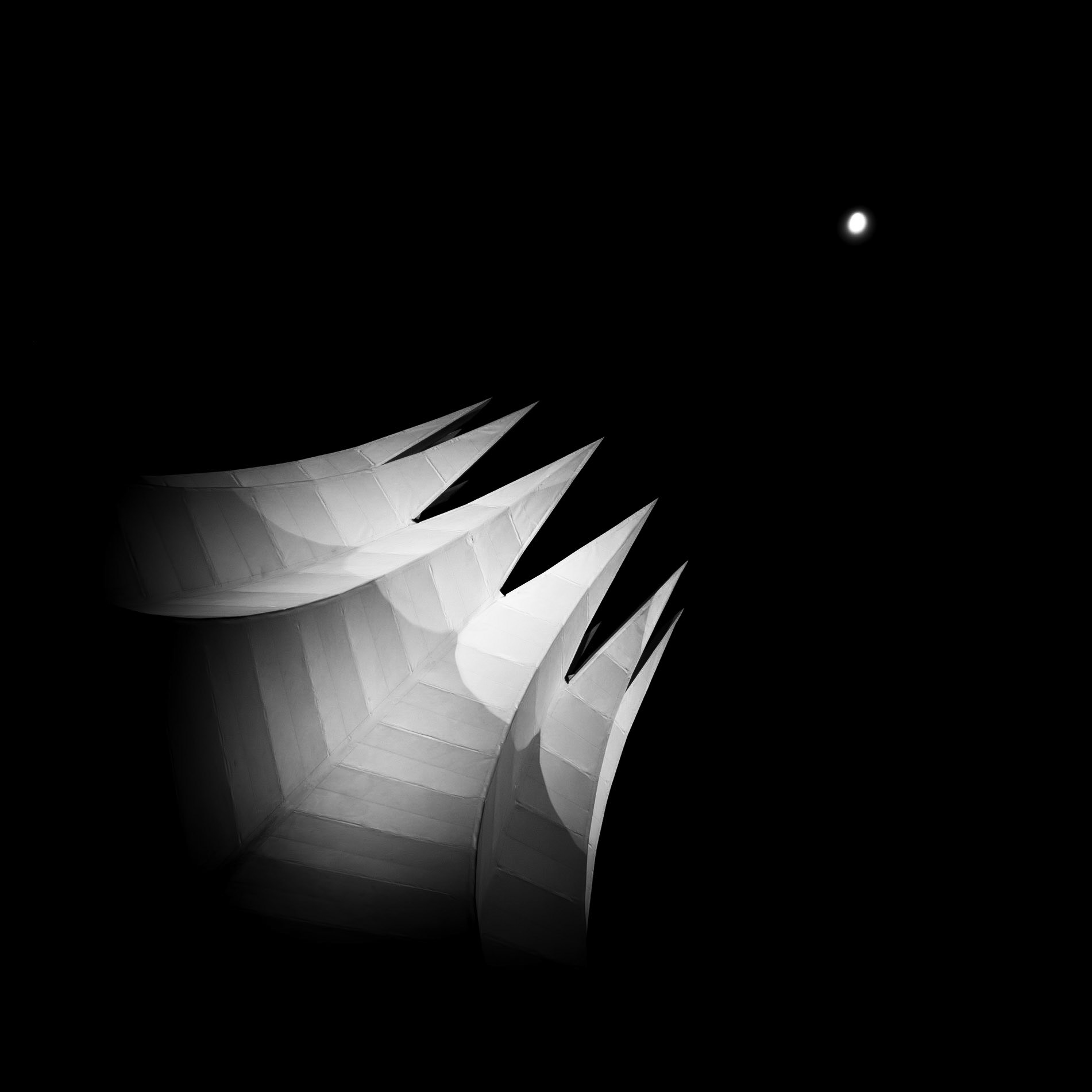 The spiked roof of the Tempodrom points towards the bright moon in a clear sky over the city of Berlin