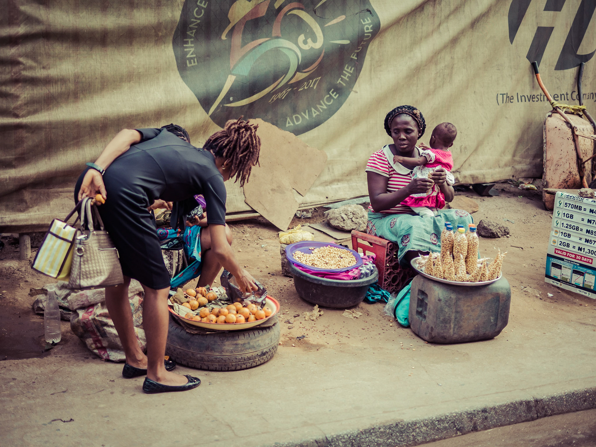 A mother with her young child watches as a competiting seller grabs a sale at a road-side market in Lagos, Nigeria