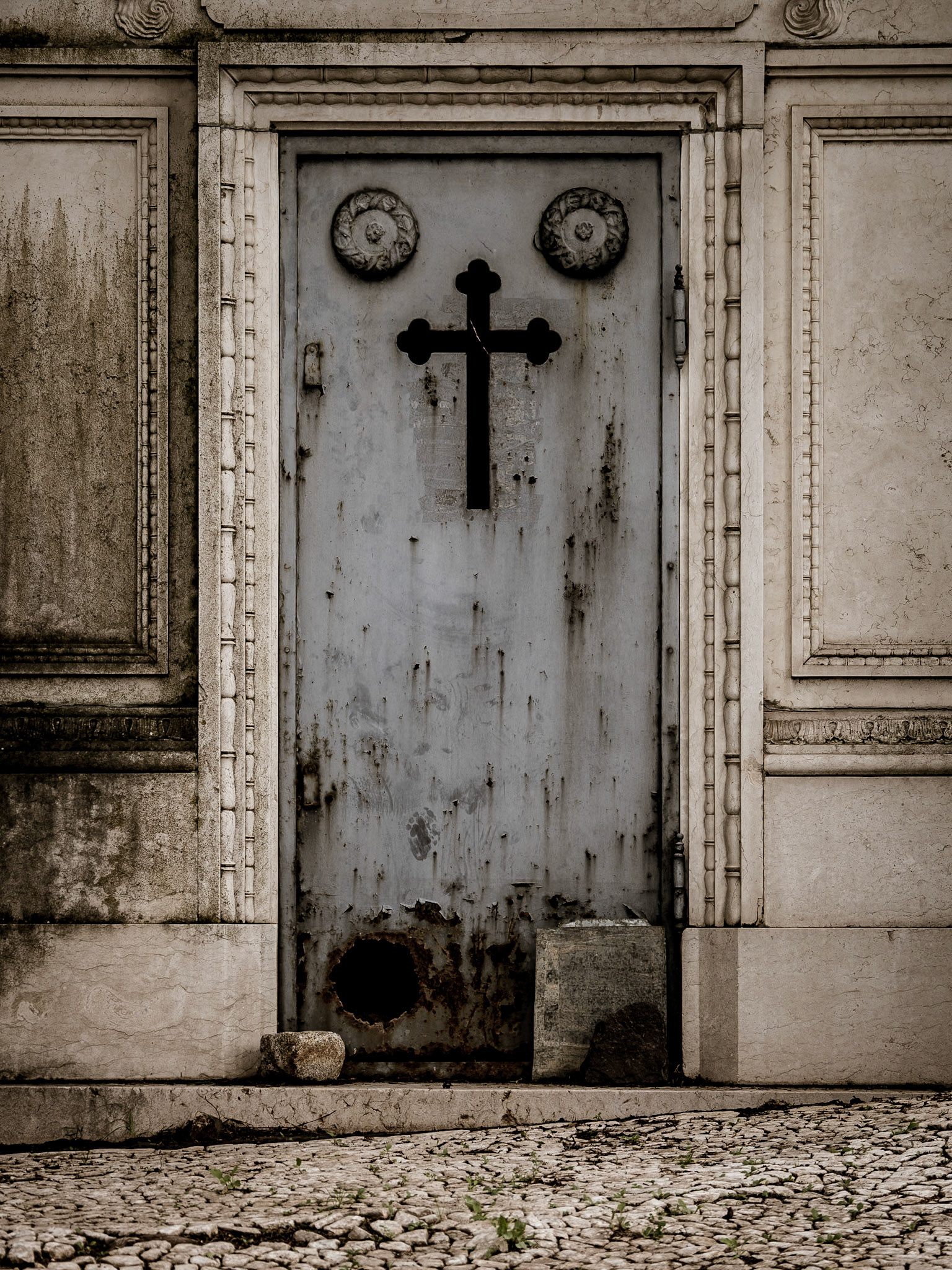 A rusty hole allows local stray cats to come and go through an iron door in the historic Prazeres Cemetery in Lisbon