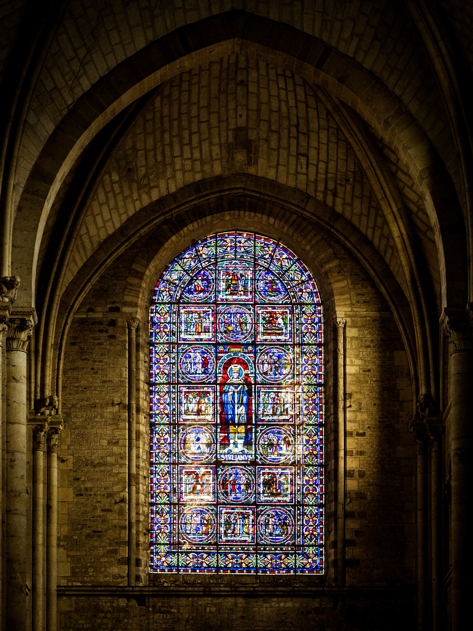 A beautiful stained glass window sits at the end of a haunting corridor in the Cathederal Saint Julien in Le Mans