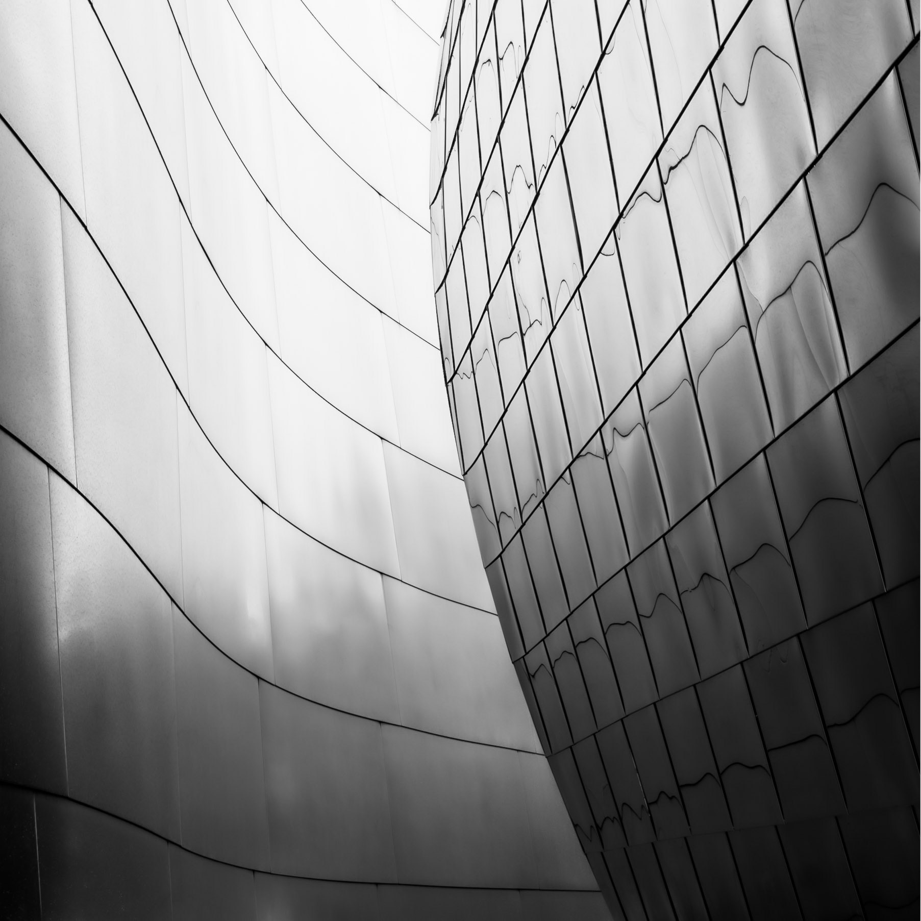 The dark line of steel panels on the side of a building guide visitors down a curving alleyway of the Walt Disney Music Hall in downtown Los Angeles