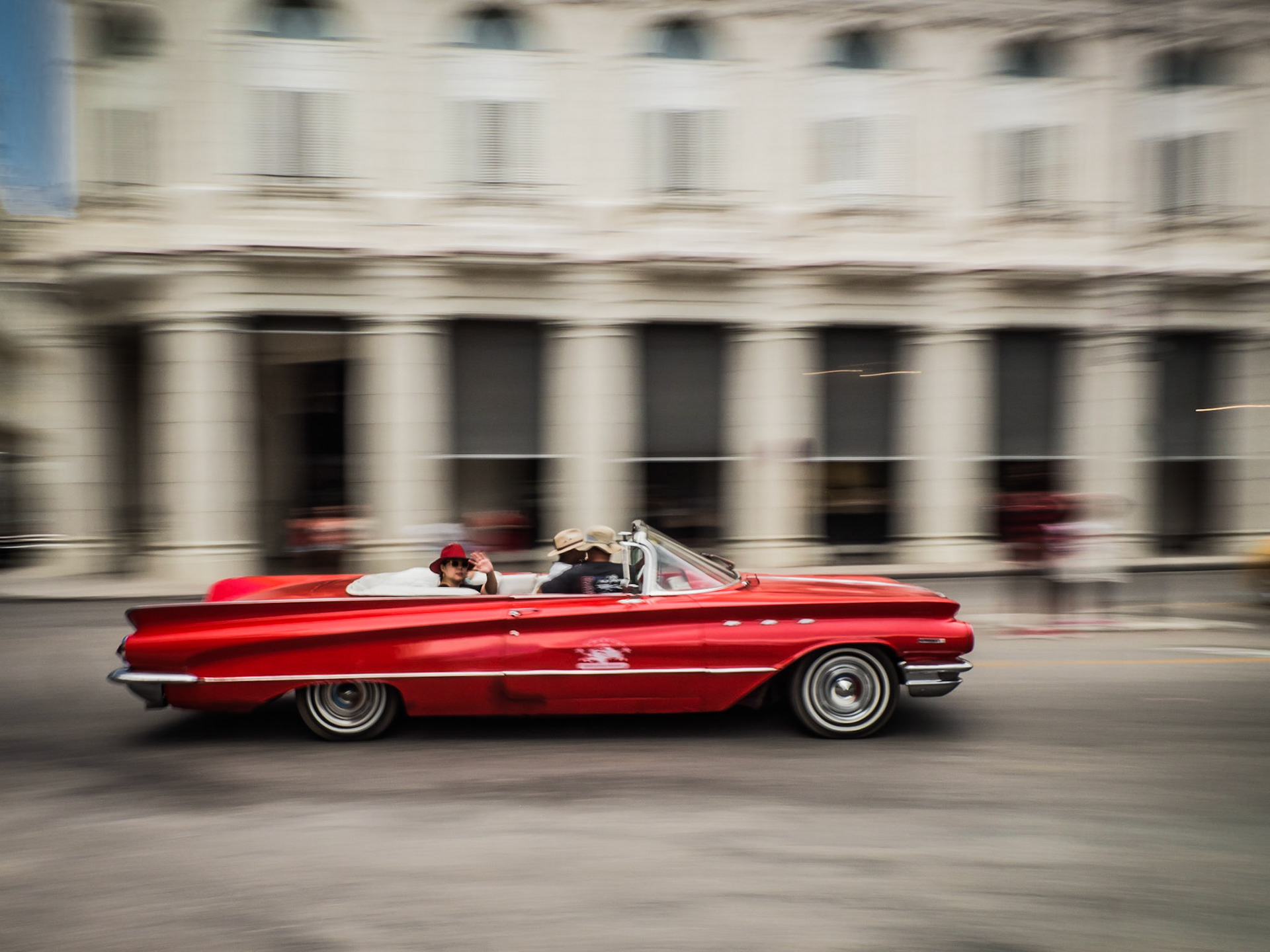A lady offers a wave as she passes by in the back of a classic car, one of many restored and now operating as taxis around the Cuban capital, Havana