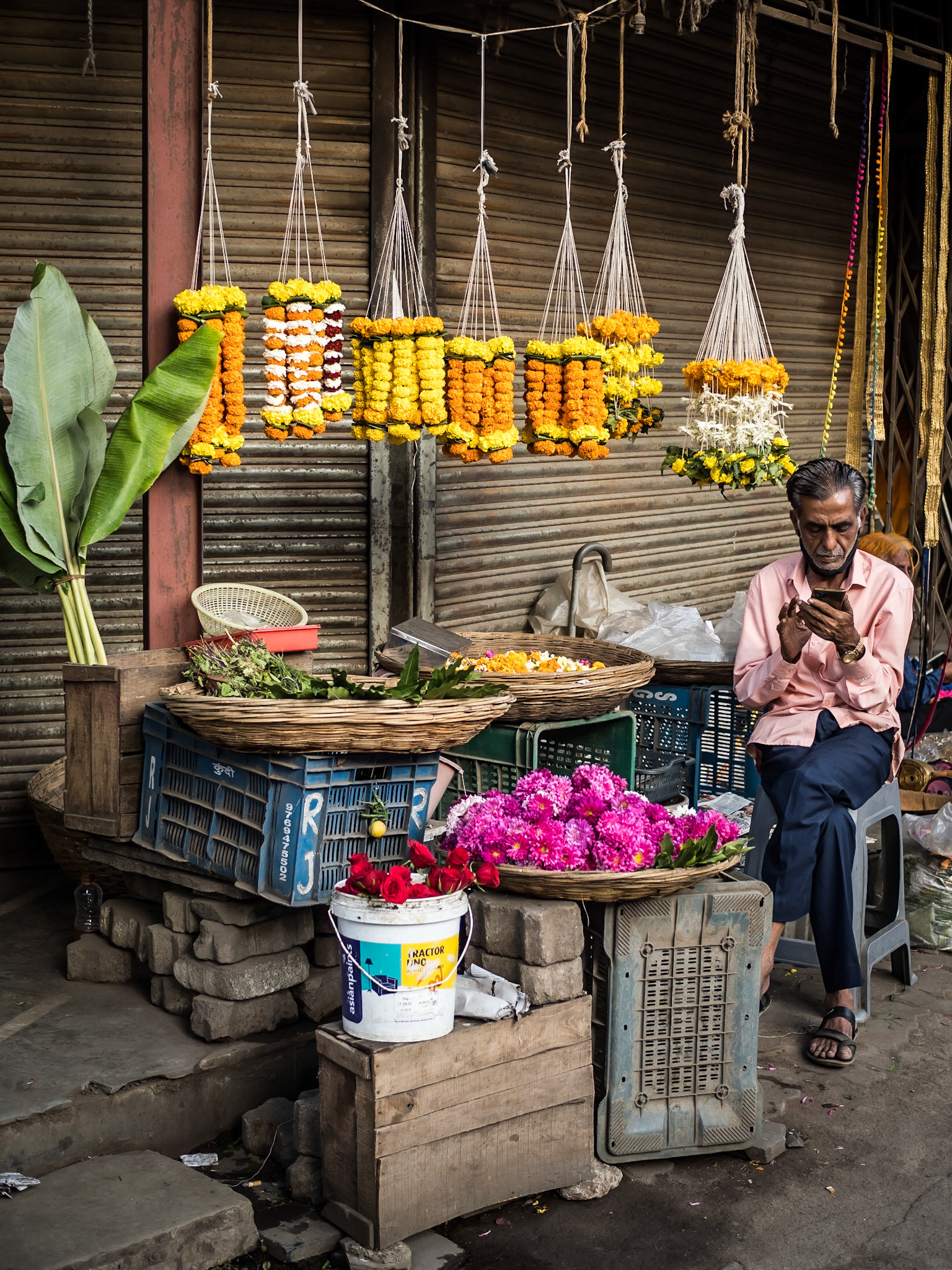A market vendor selling garlands of flowers catches up in during a lull in sales at a Mumbai street market