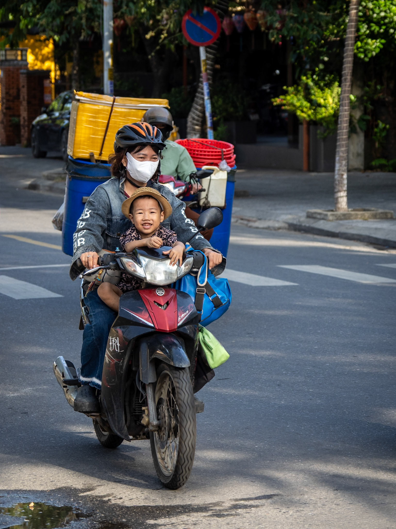 On the main street through Hoi An in Vietnam a young boy flashes a cheeky grin when he spots the camera on his journey to school