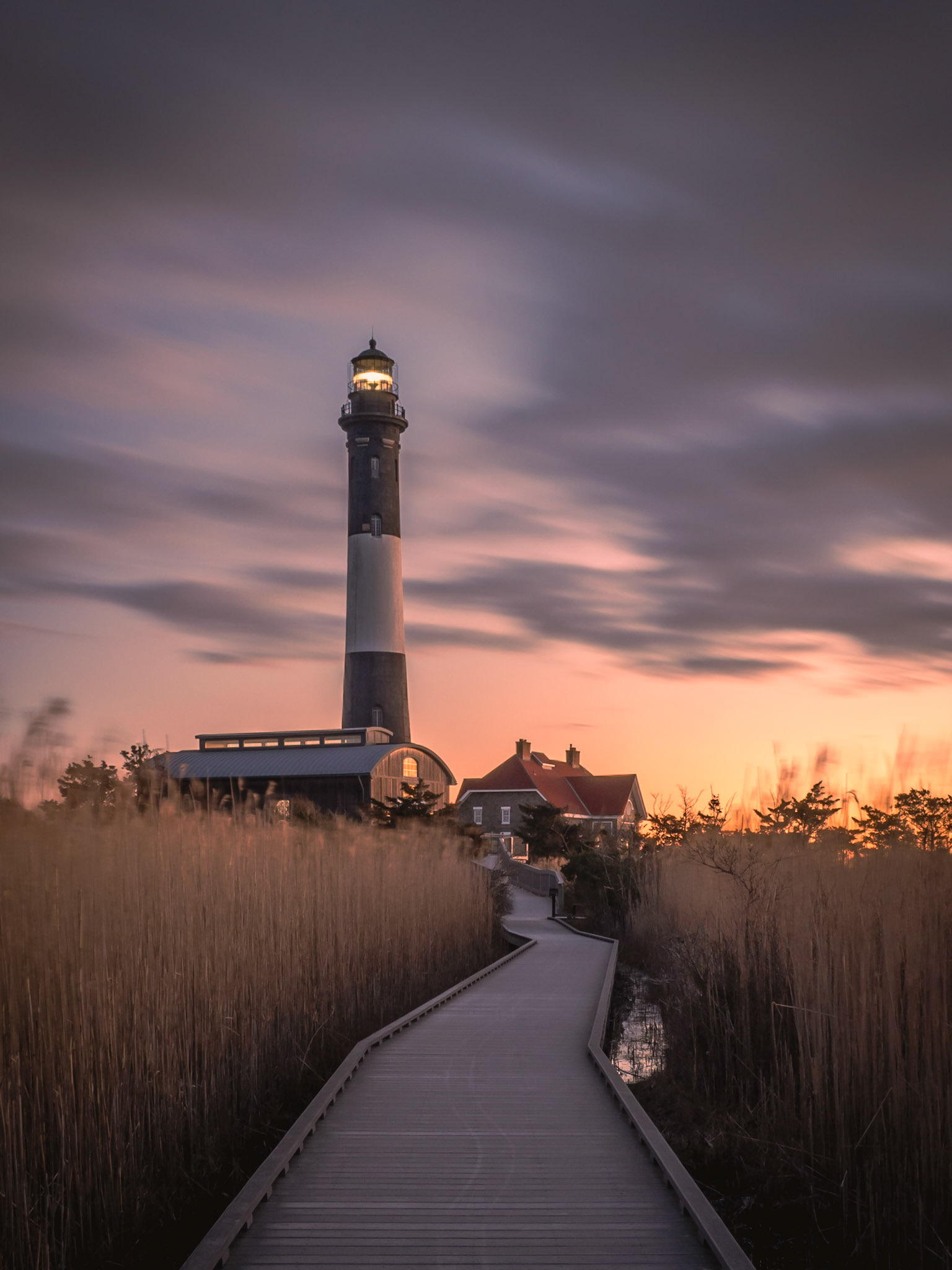 Clouds race by in the sky as dawn rises behind the lighthouse on Fire Island