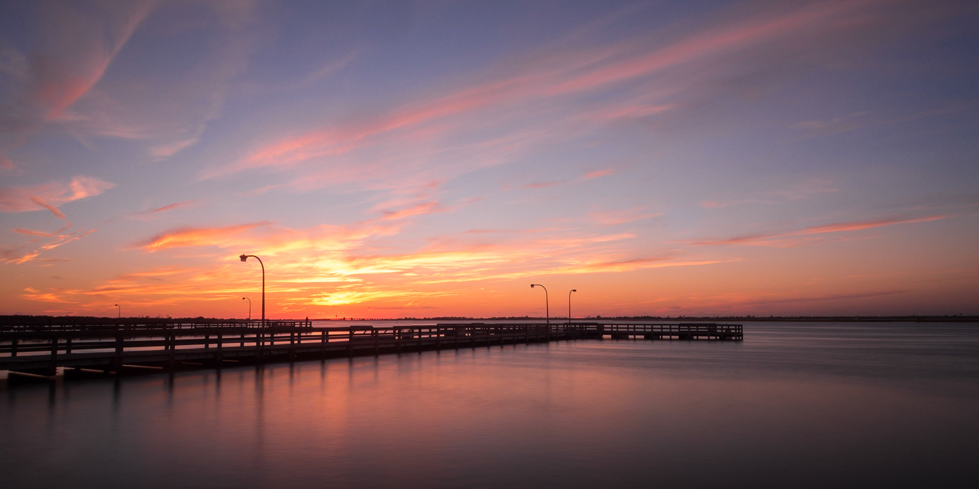 A dramatic sky with beautiful golden hues sets behind fishing piers on Jones Beach