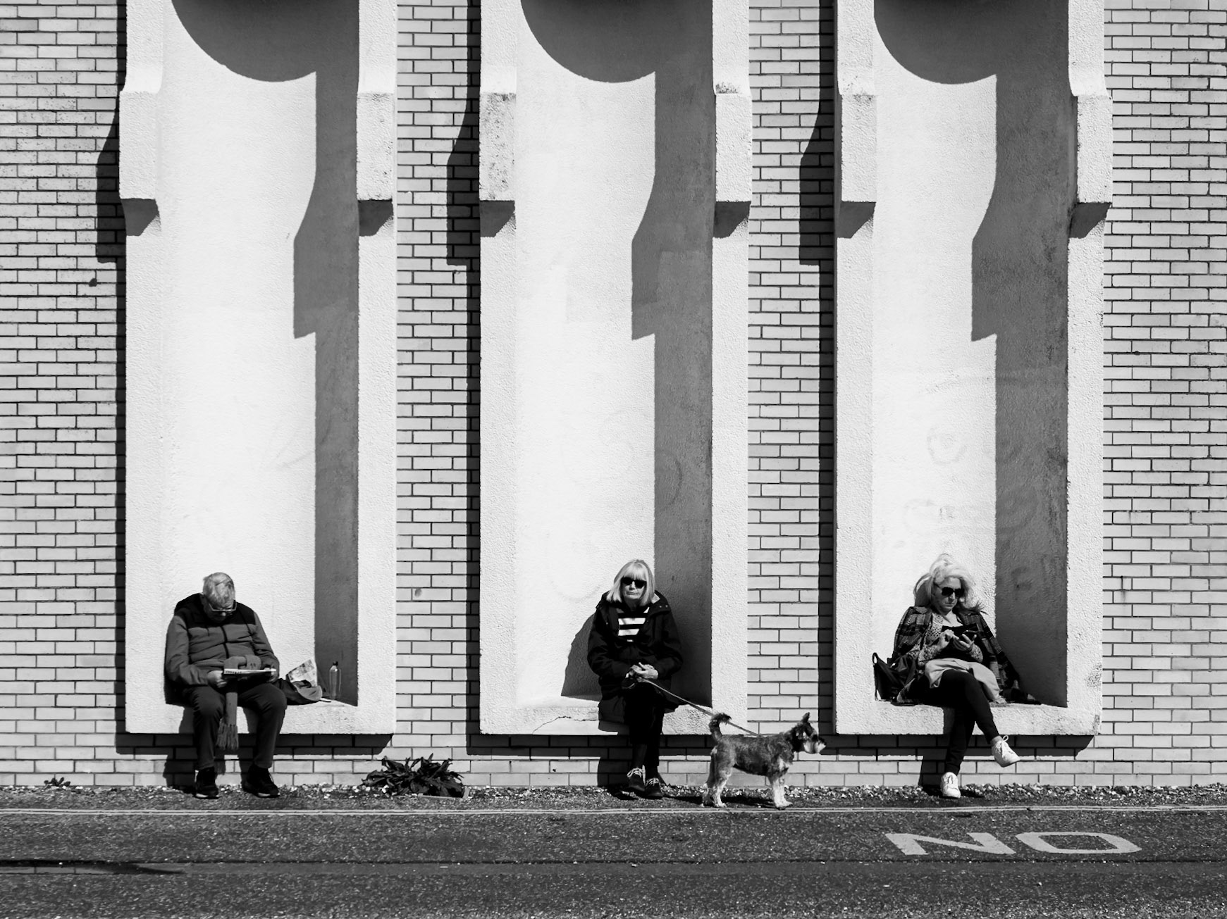 A group of walkers each sit in their own alcove, protected from the wind on a breezy Hove seafront