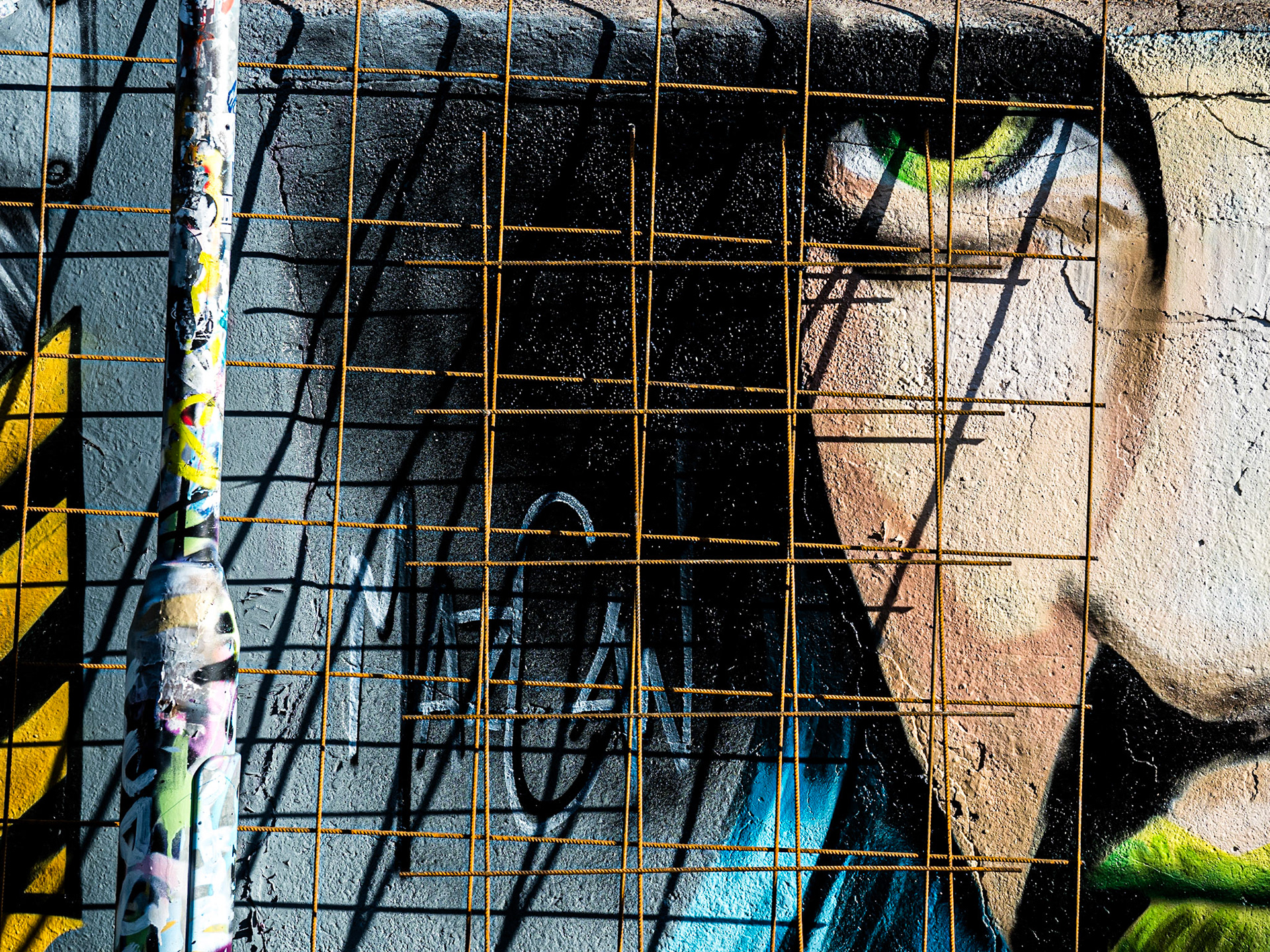 The eye of a mural looks warily through an abandoned grid of steel in Brighton's graffiti-filled Trafalgar Lane