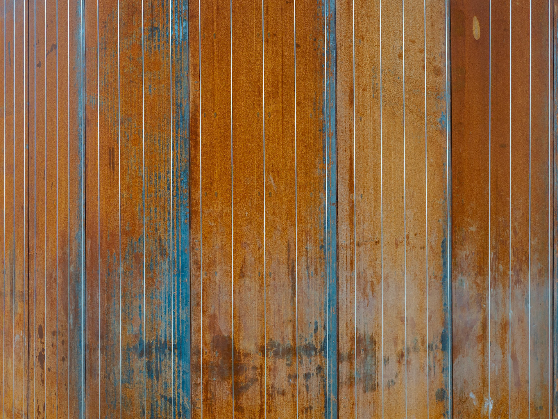 Metal cords hang vertically against a sheet of rusting iron