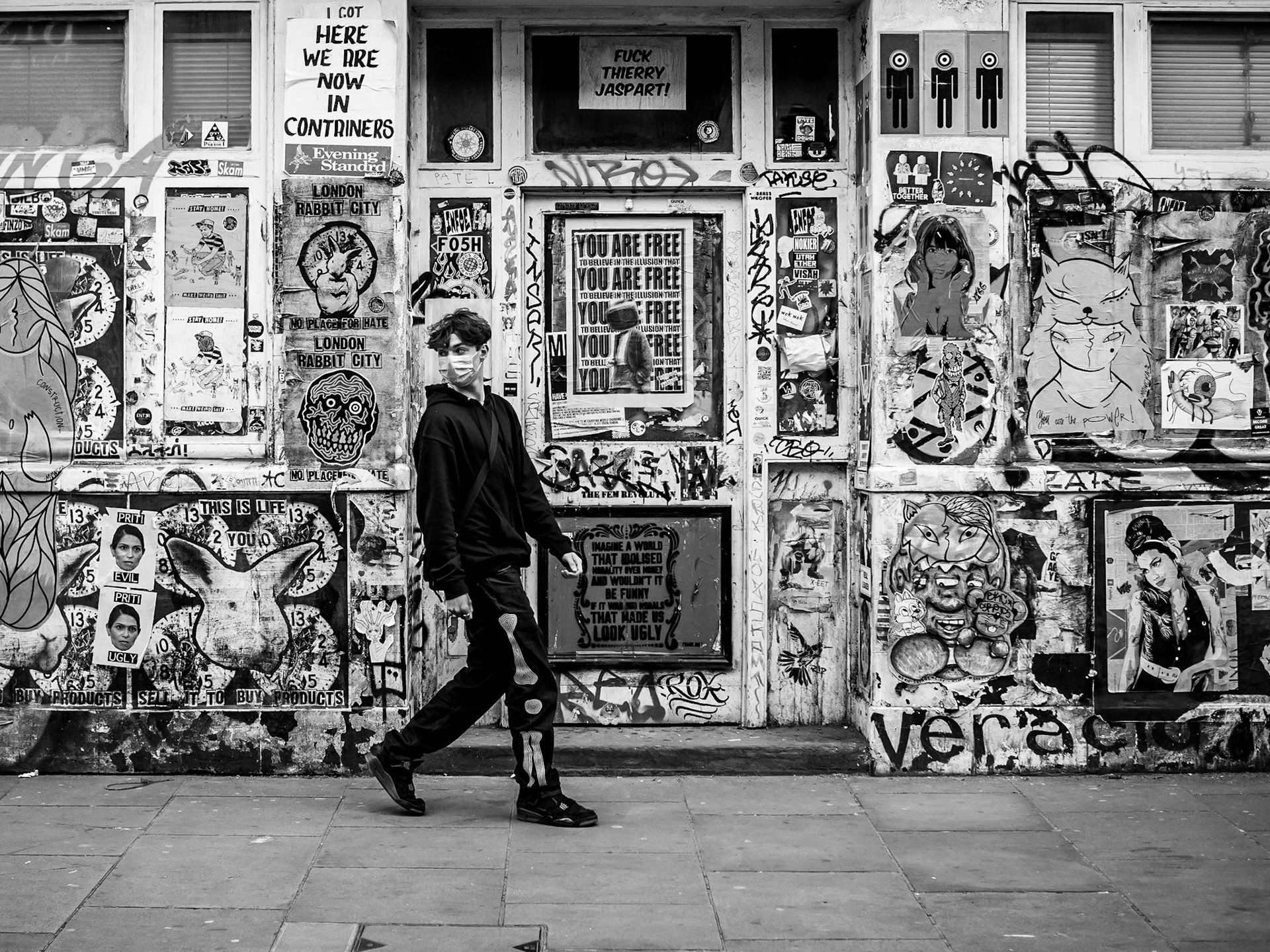 A passer-by blends in with the mass of posters and graffiti behind him as he strolls down Brick Lane in London