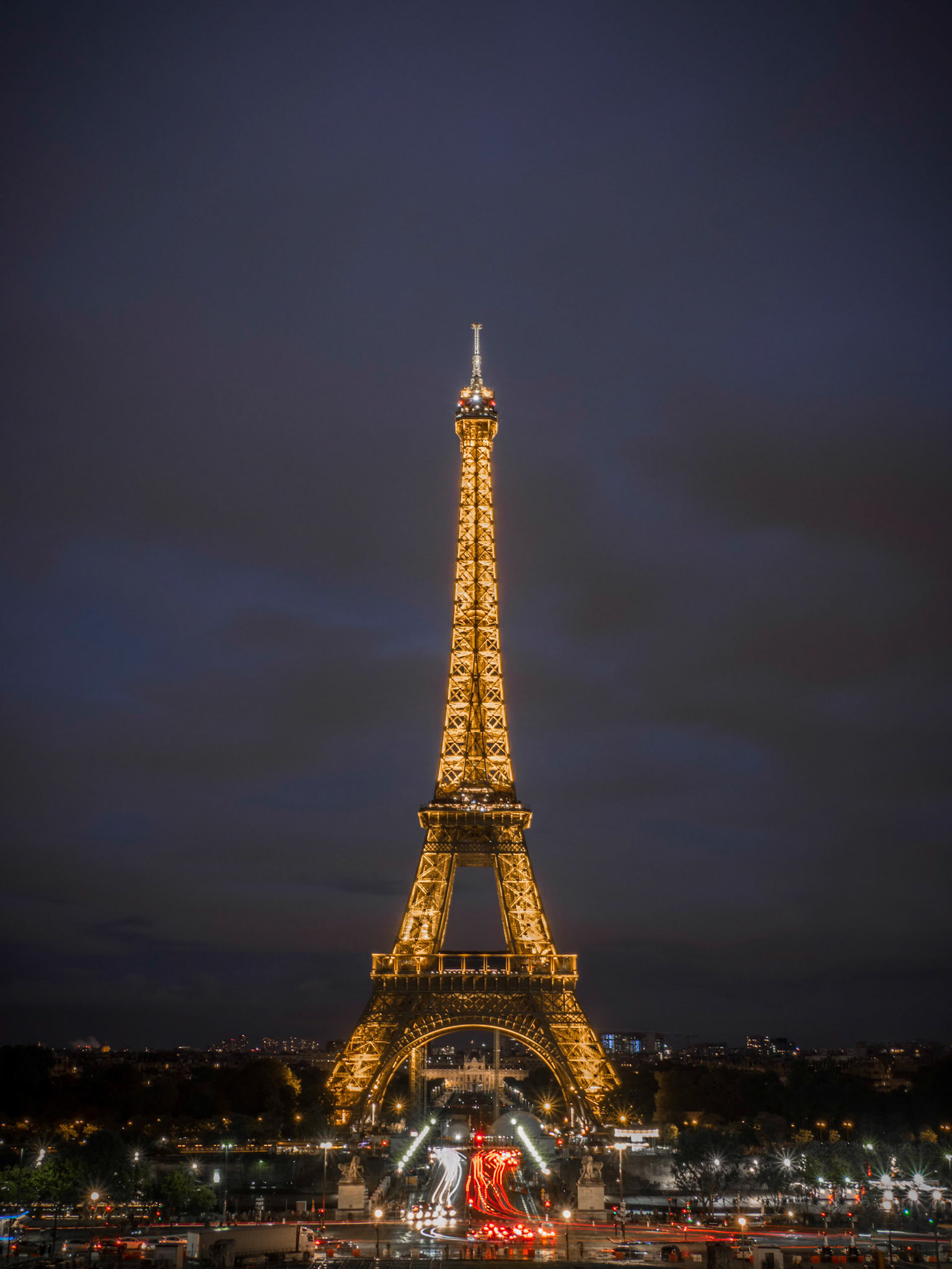 Rush-hour traffic form trails of light as the iconic Eiffel tower stands magnificent as dusk falls over Paris