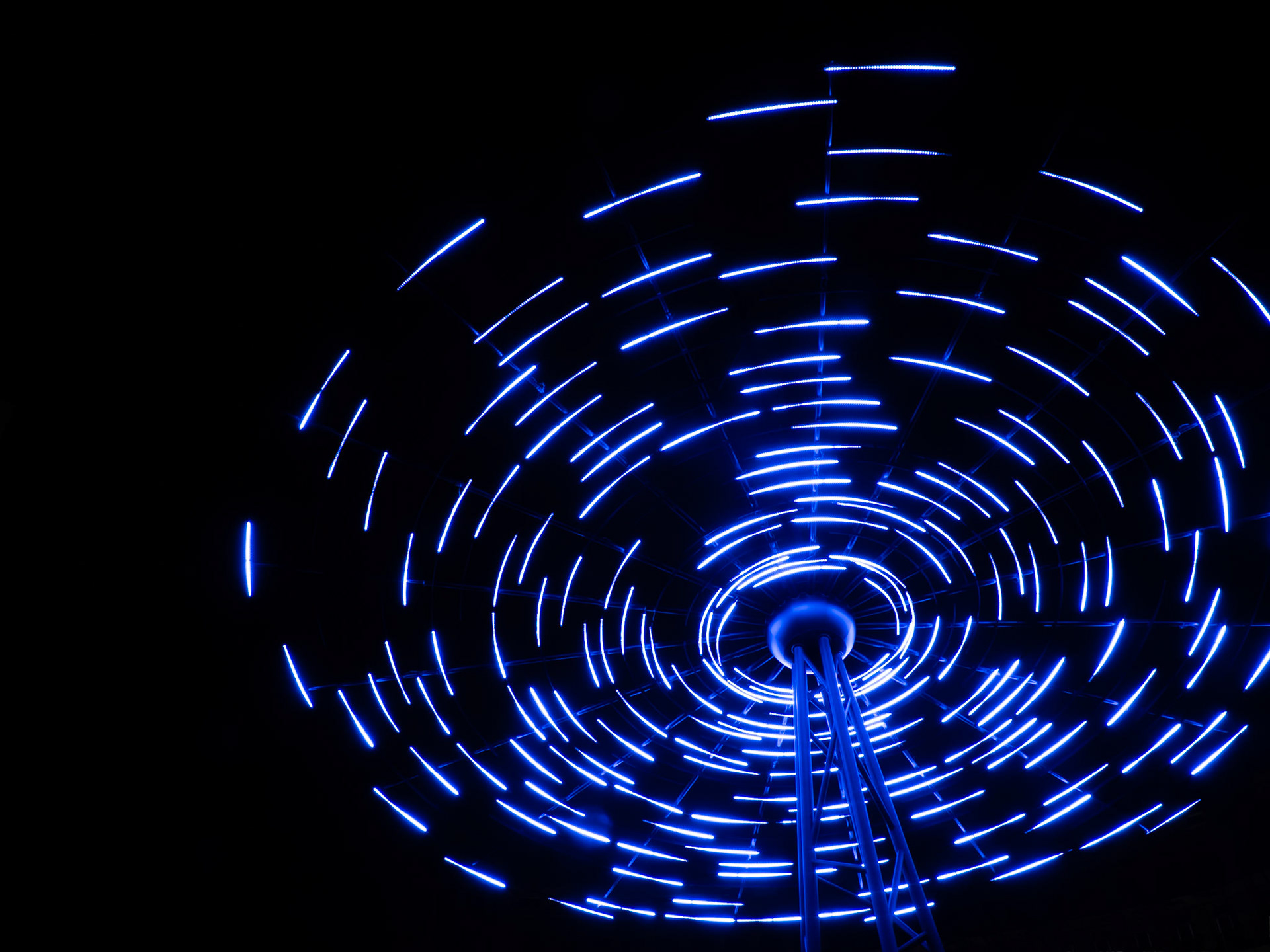 A hypnotic dance of electric blue lights, captured in a long exposure, paints a mesmerizing spiral against the velvet cloak of night