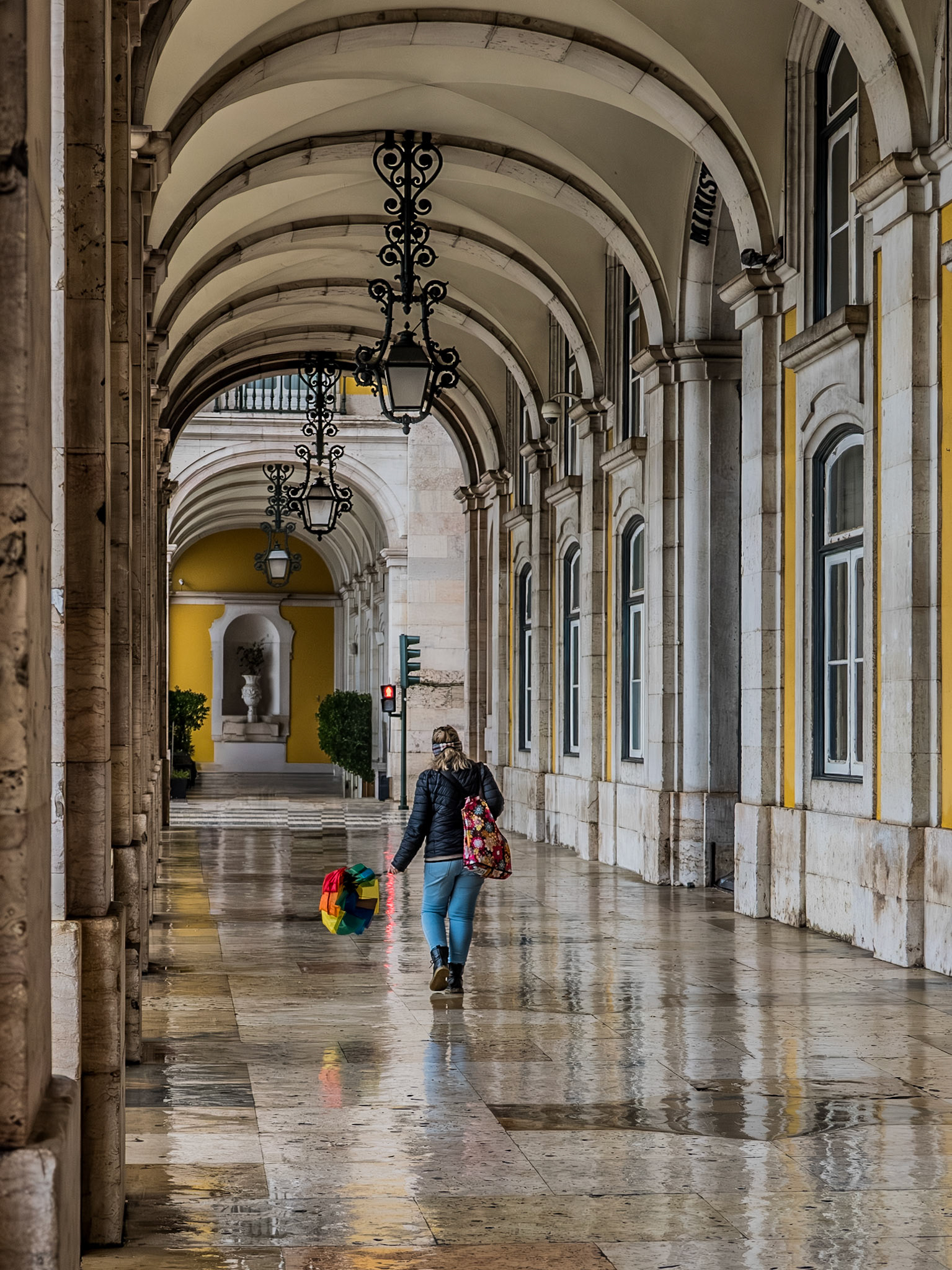 A solitary walker carrying a colourful umbrella passes beneath the grand vaulted stone arcades of Commerce Square in Lisbon