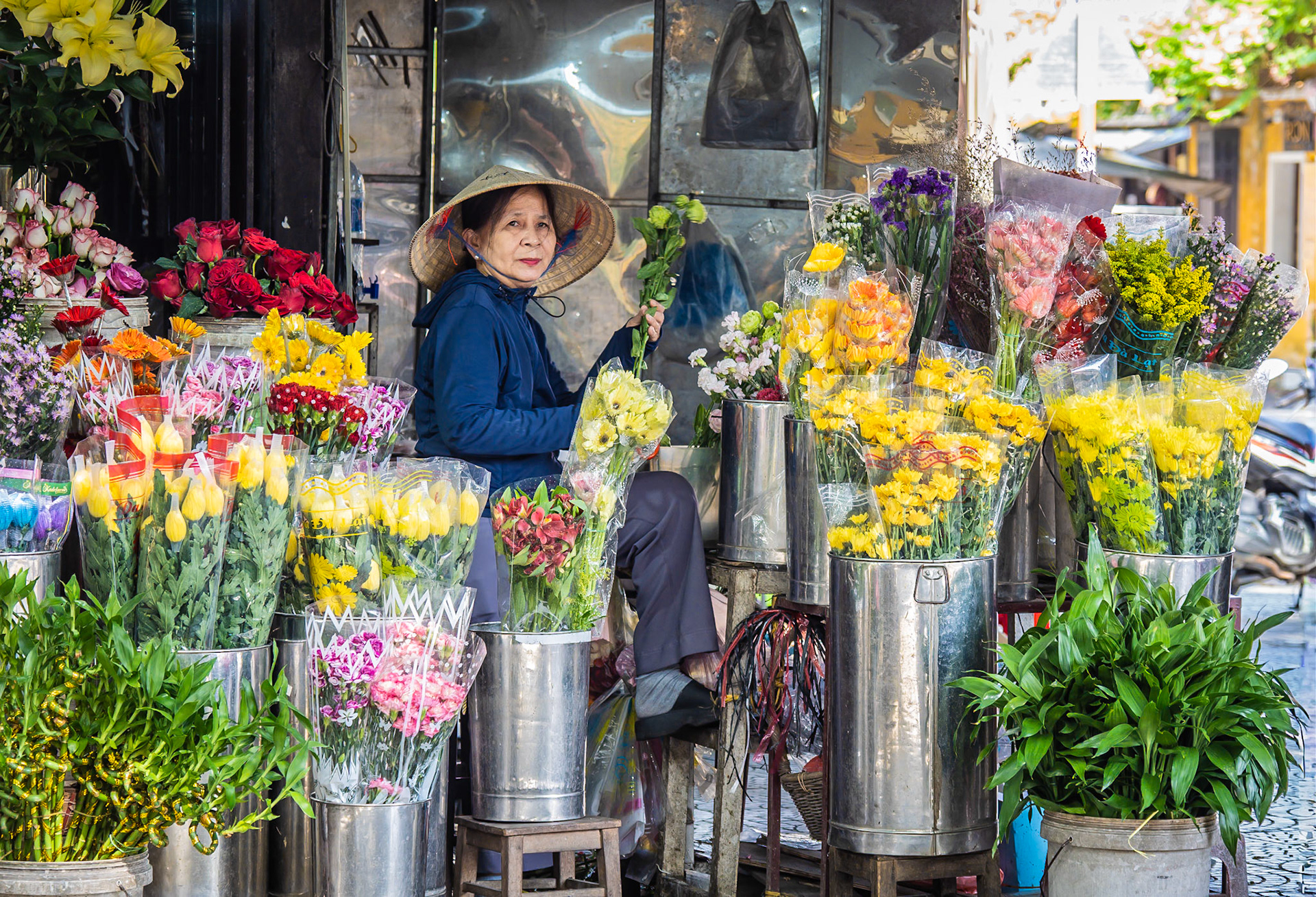 Wearing a traditional Non La hat and surrounded by a vast array of vibrant flowers, a florist prepares for the busy day ahead in Hoi An in central Vietnam
