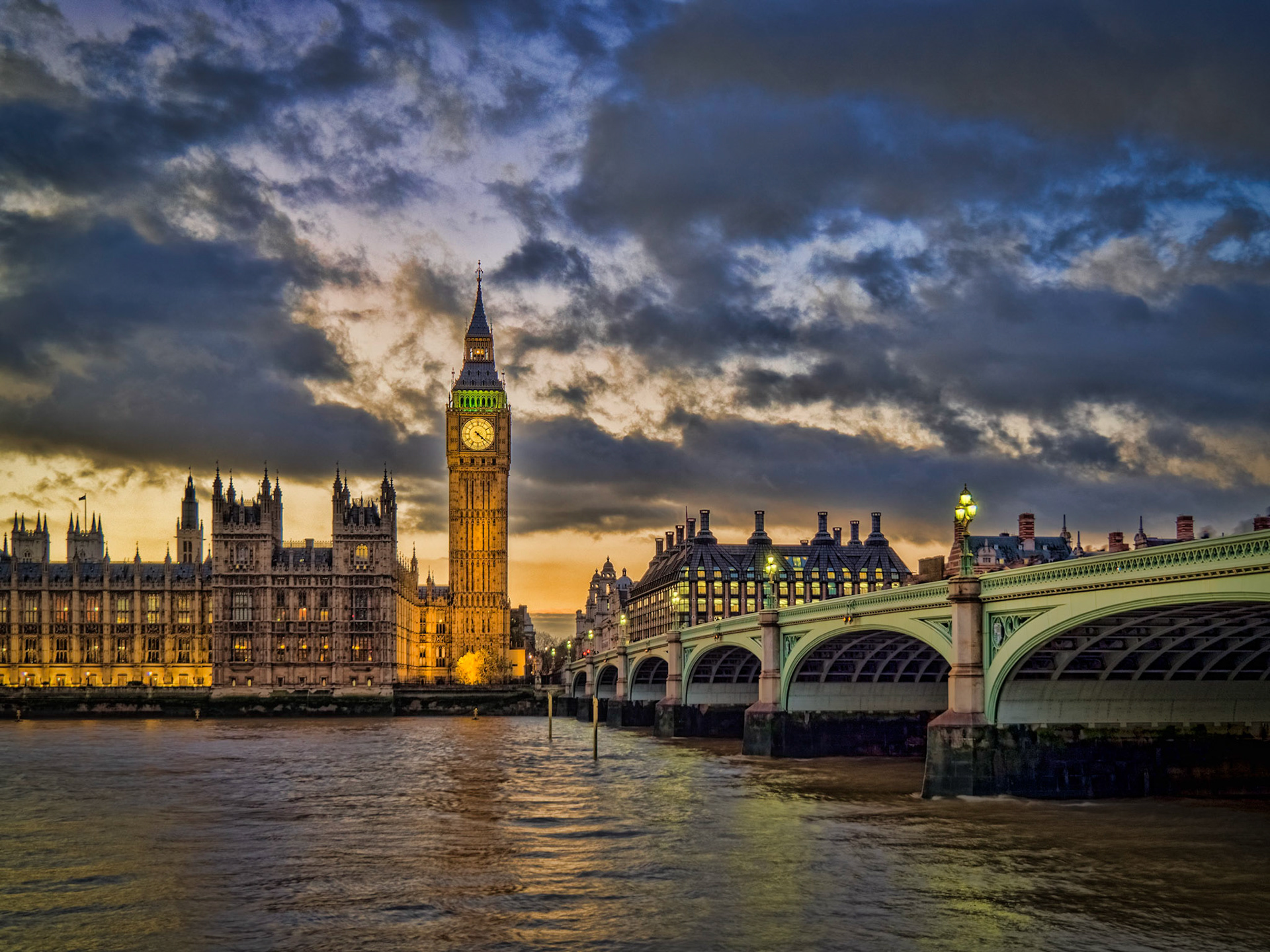 The tower of Big Ben sits at the end of Westminster Bridge as the sun sets through a moody sky over London